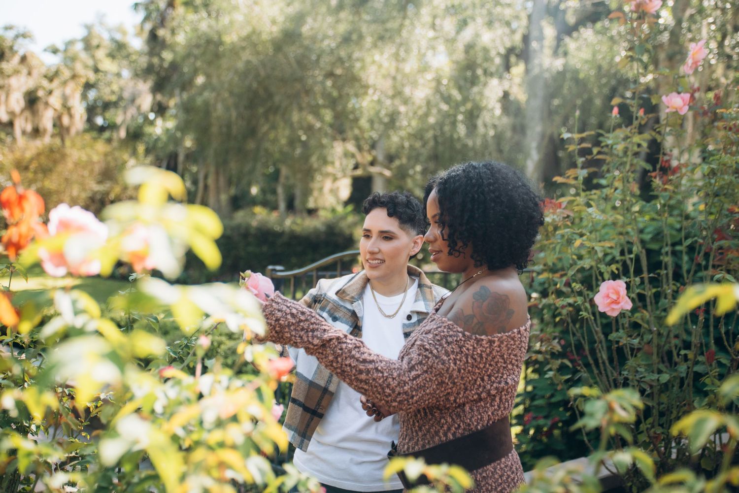 Couple sharing intimate moments among blooming flowers in a sunlit garden.