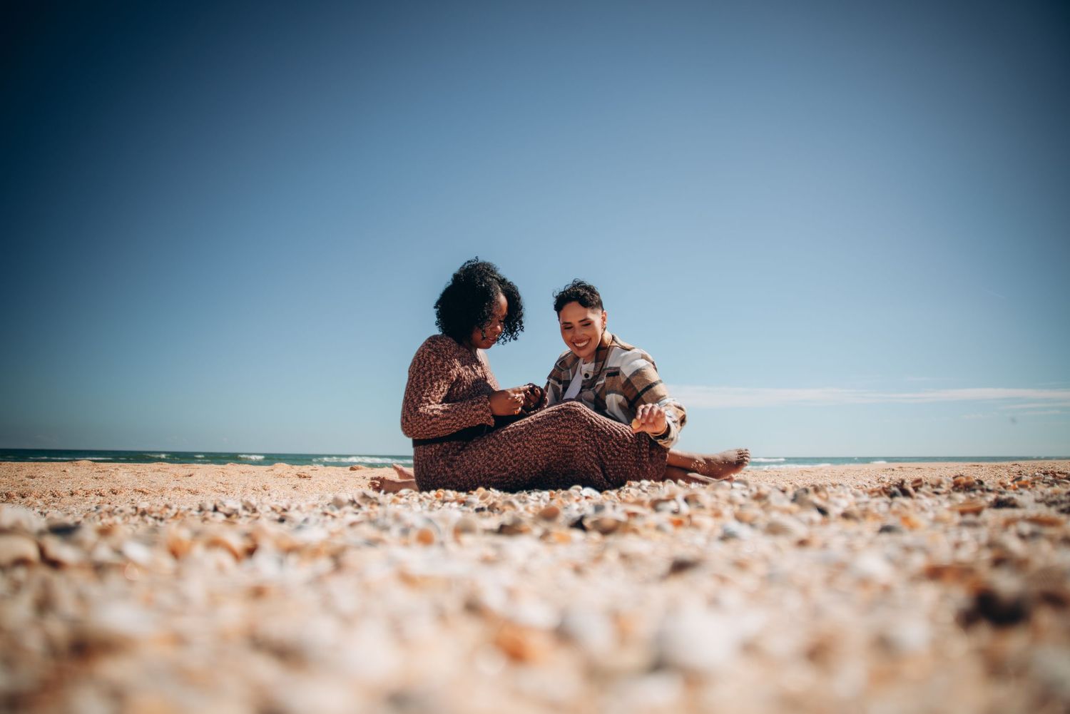 A couple sits intimately on a sandy beach with the ocean horizon in the distance.