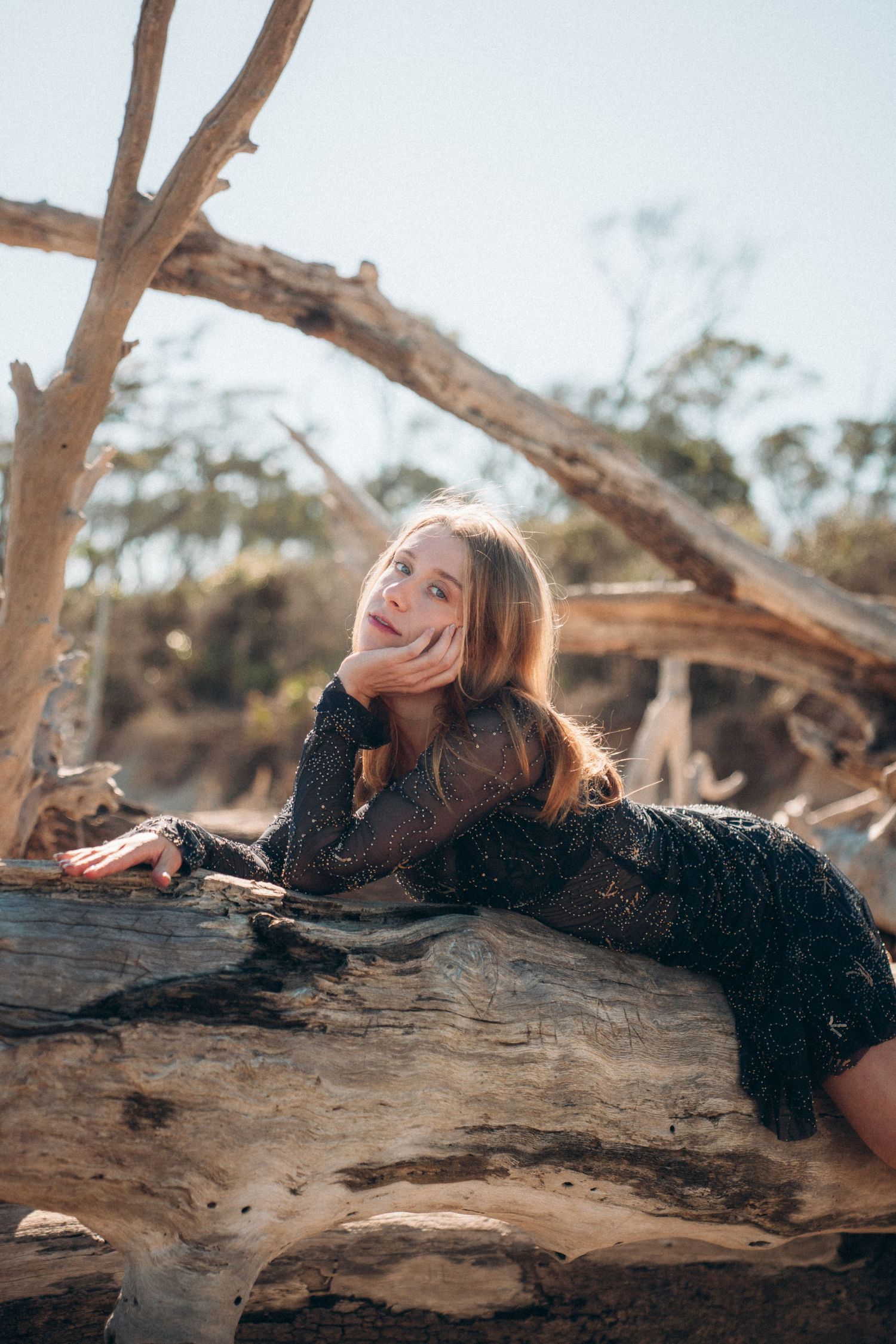 A person in a black dress lying on a fallen tree trunk in a natural outdoor setting.