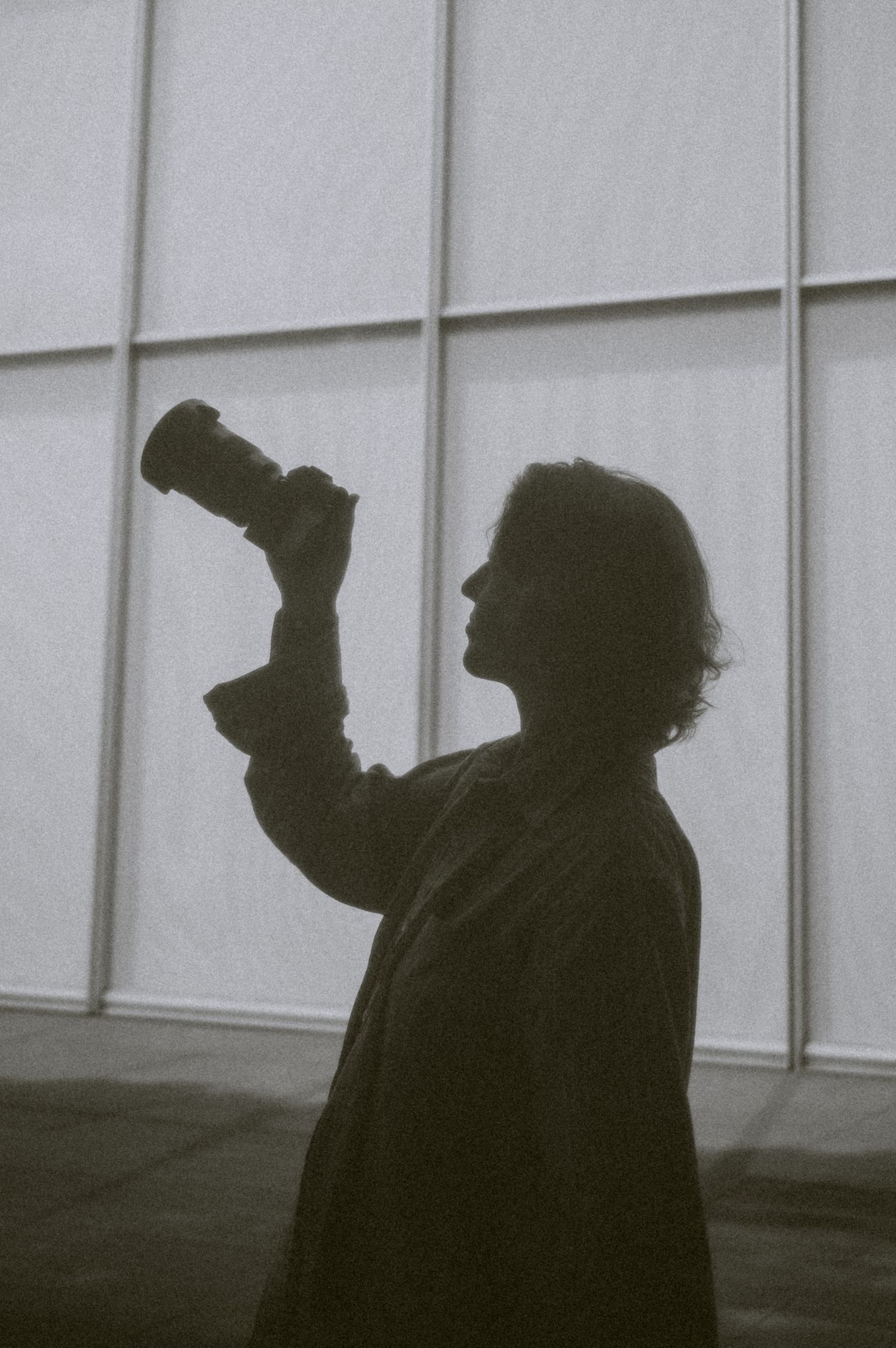 Silhouetted figure sequence against white wall in moody black and white composition.