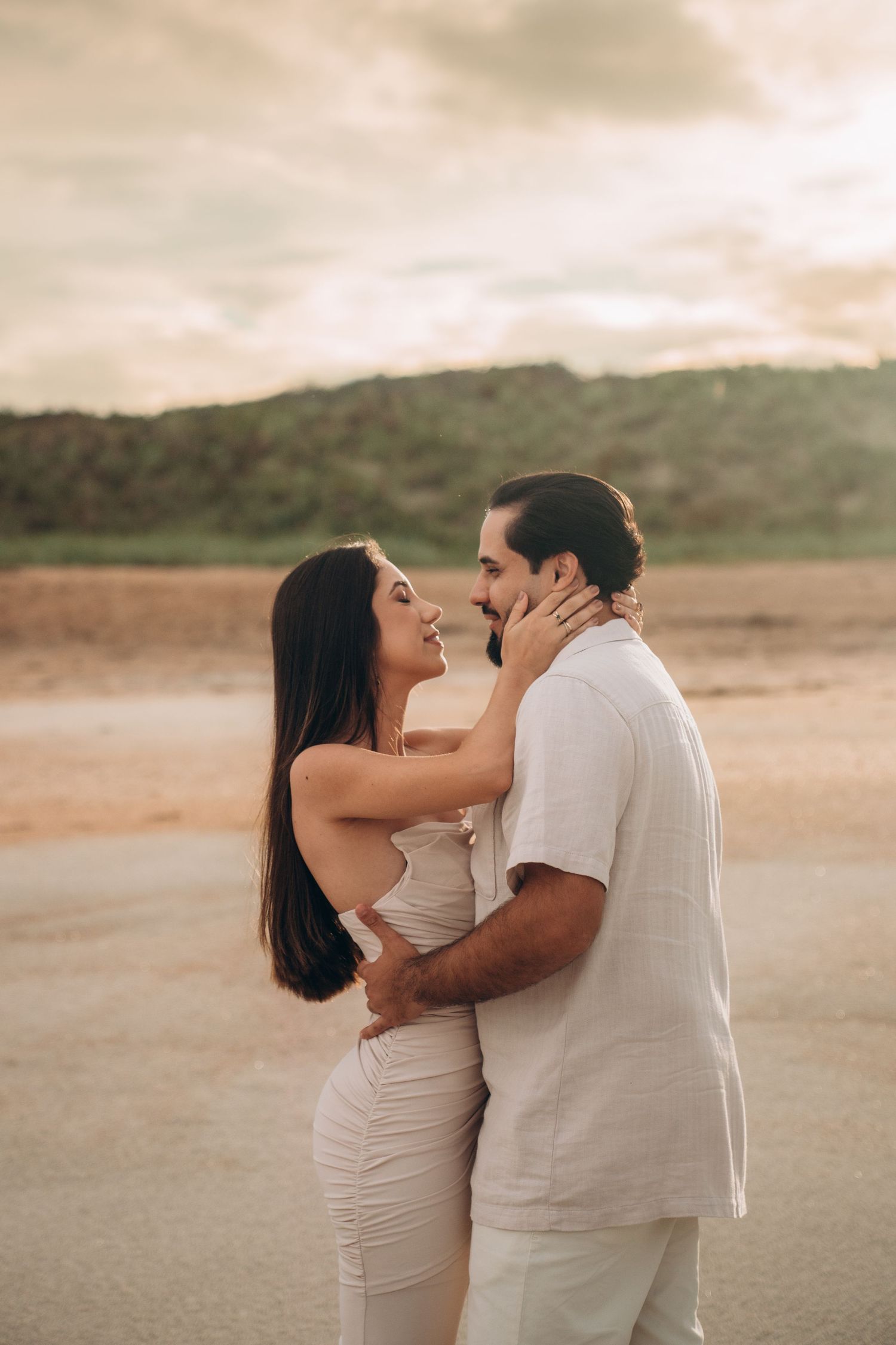 Romantic couple embracing during sunset photoshoot on sandy terrain.