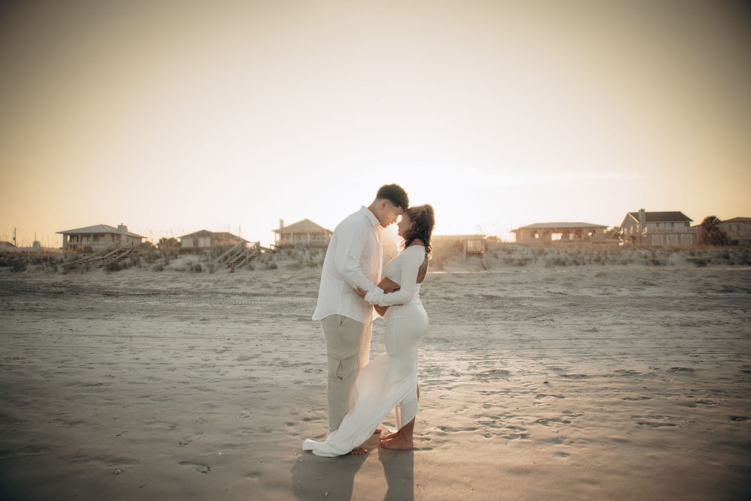 Sunset beach maternity session with coastal homes visible in the background.
