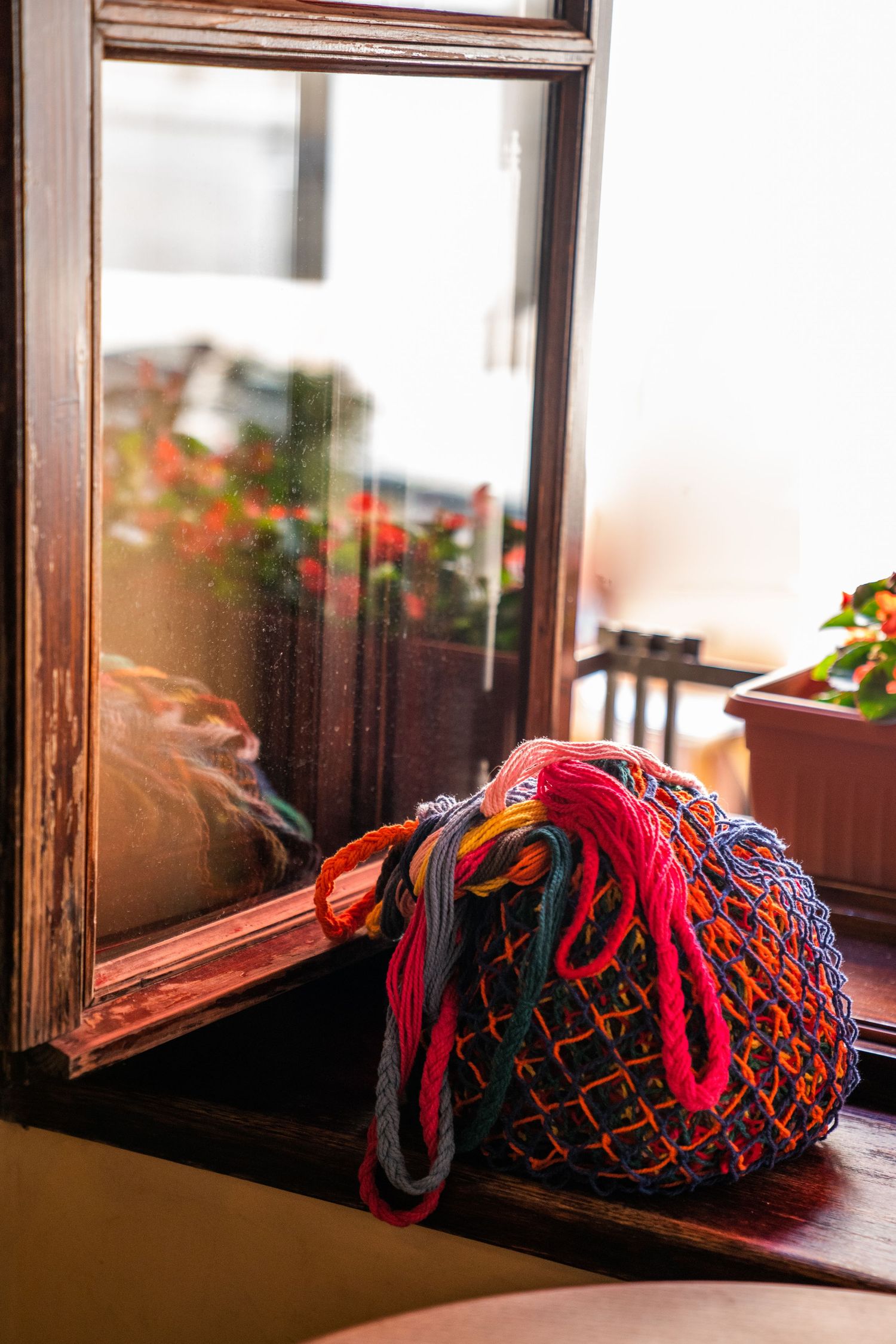 Vibrant multicolored crochet mesh bag resting on a wooden windowsill by a glass window.