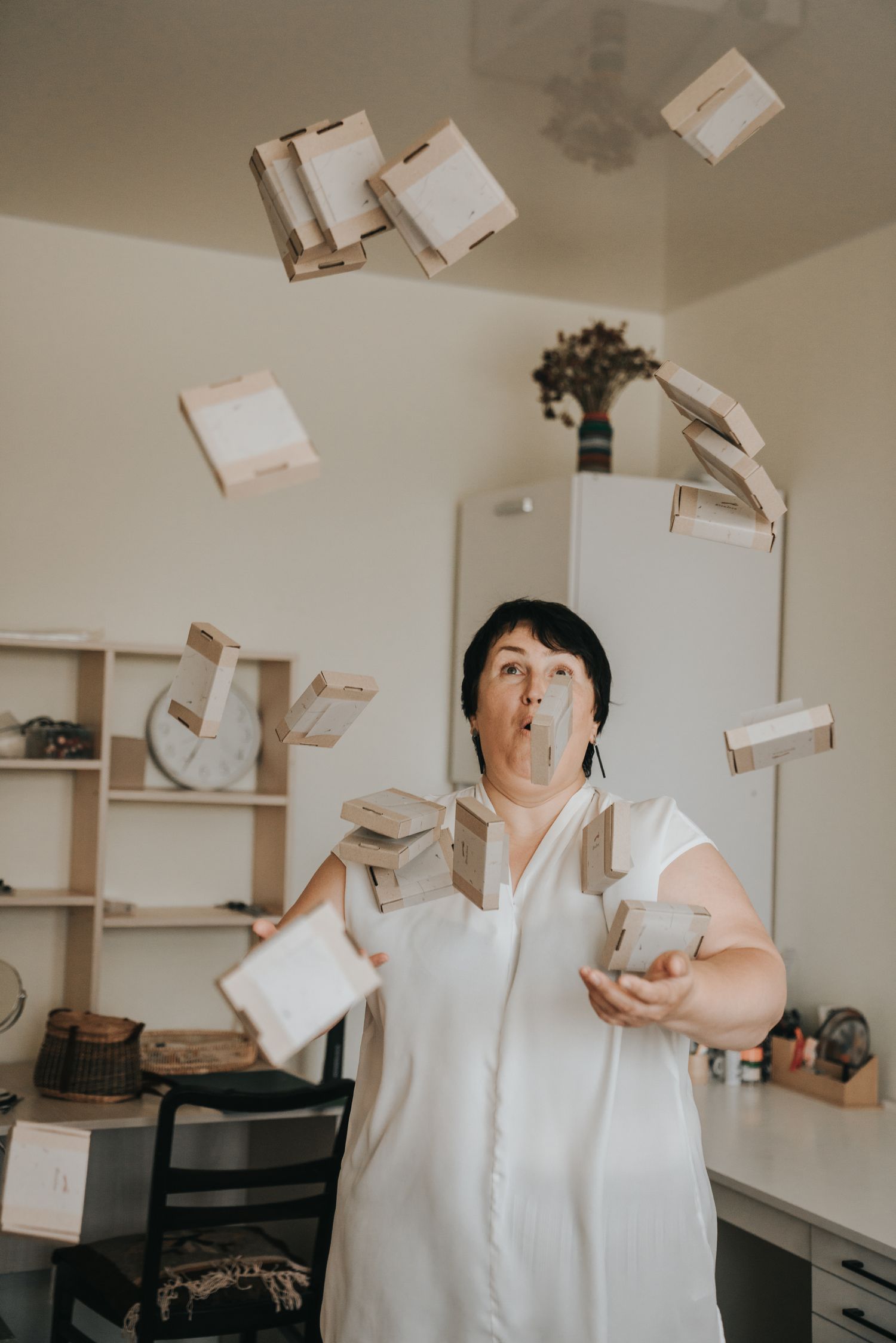 Woman in white dress tossing cardboard boxes in the air inside a bright modern room.