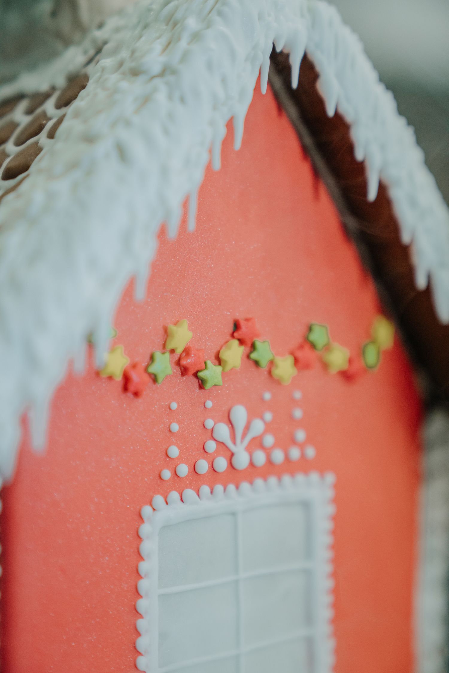 Close-up of a decorative red gingerbread house with white icing, colorful star sprinkles, and snow-covered roof.