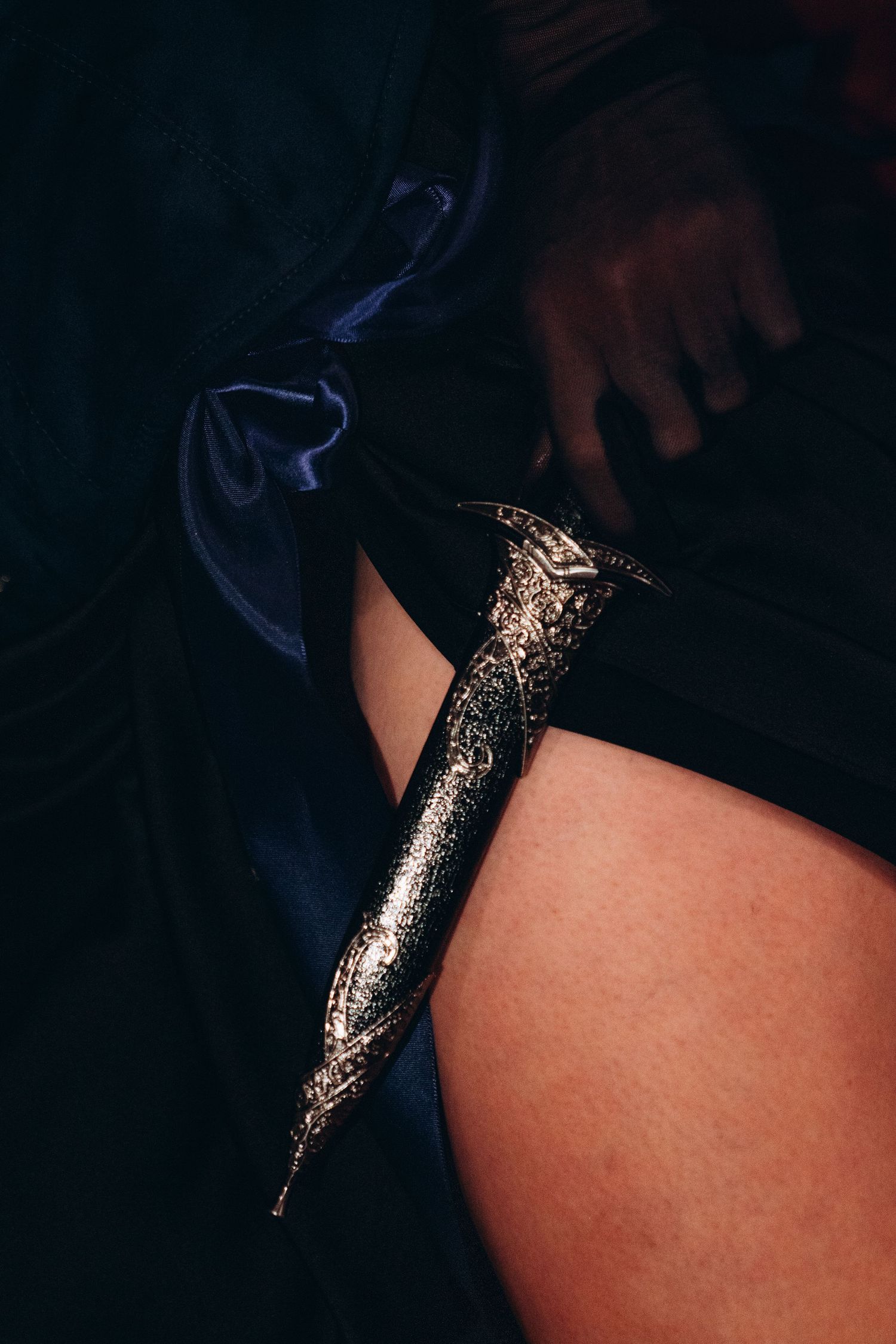 Ornate gold dagger resting against a leg draped in dark blue satin fabric.