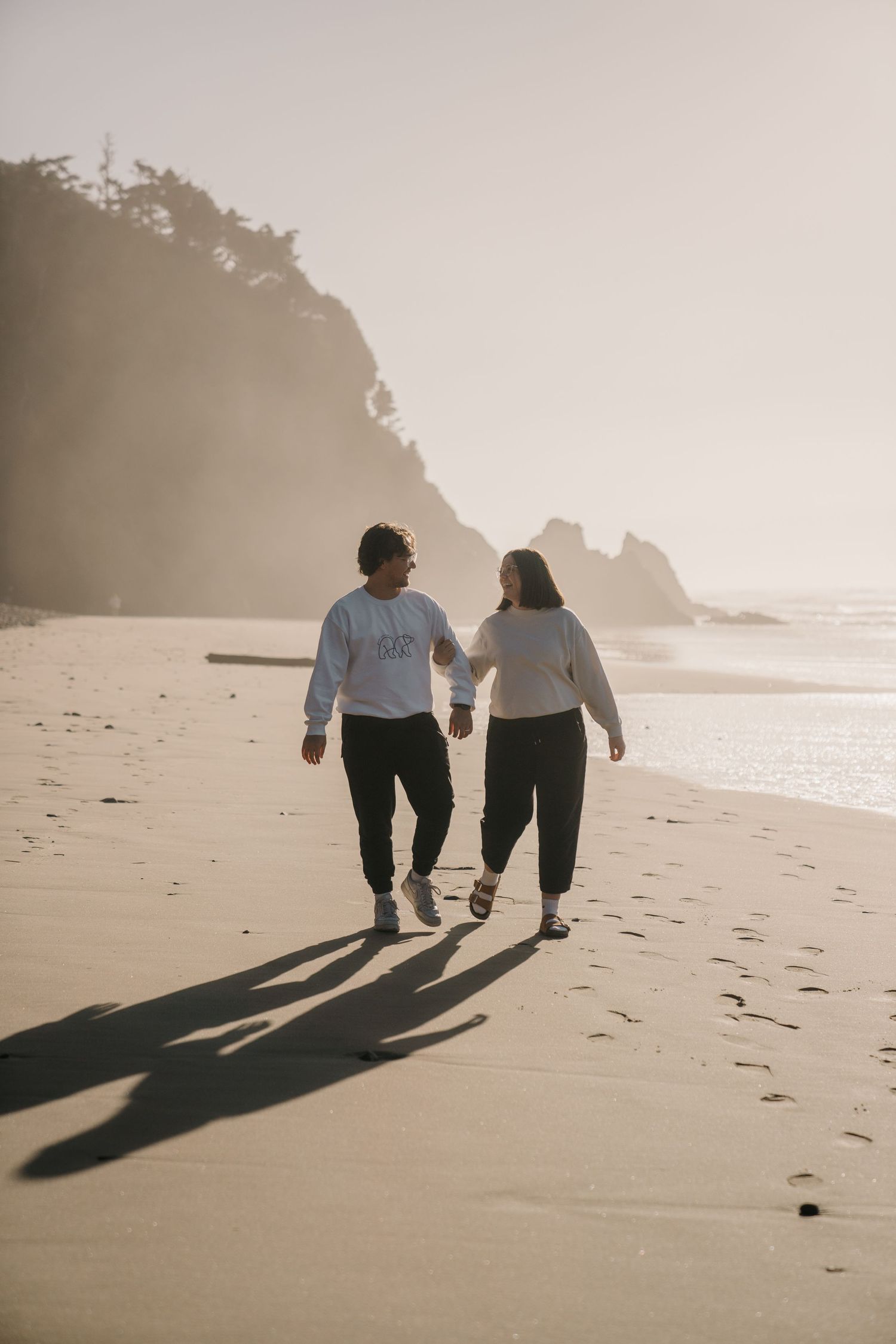 Two people walking on a beach casting long shadows in the evening light.