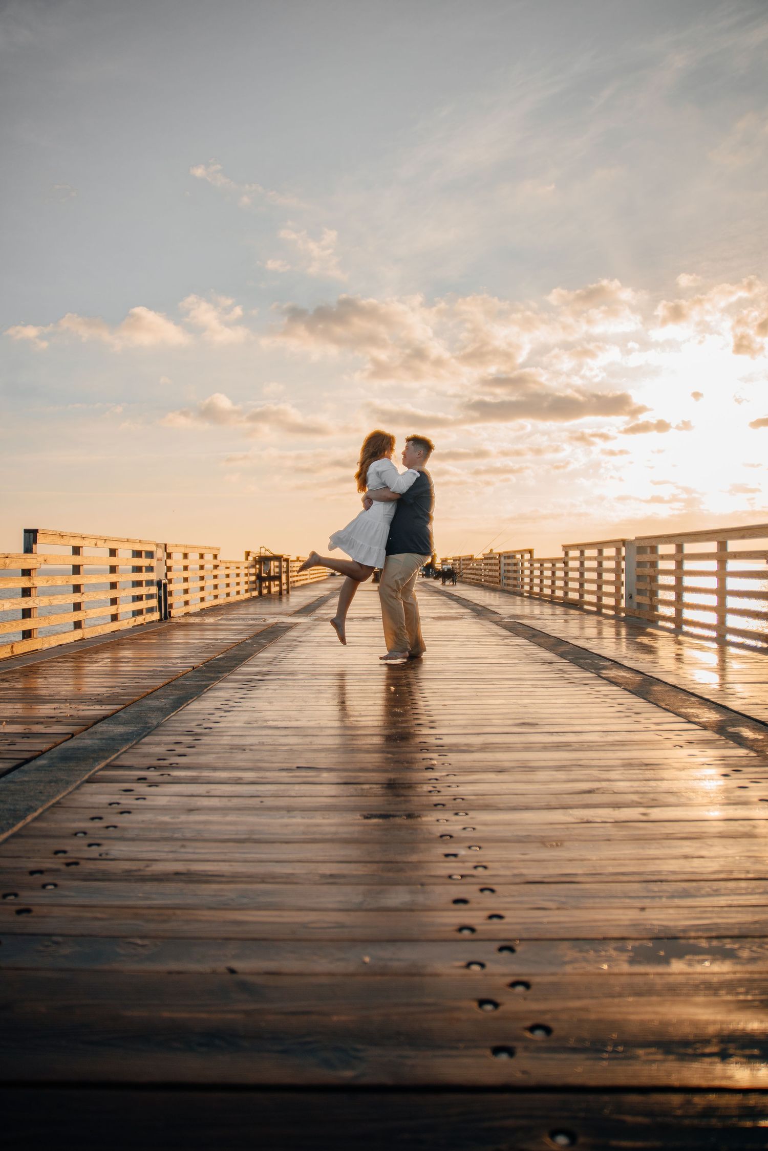 A couple stands together on a wooden pier during a beautiful sunset.