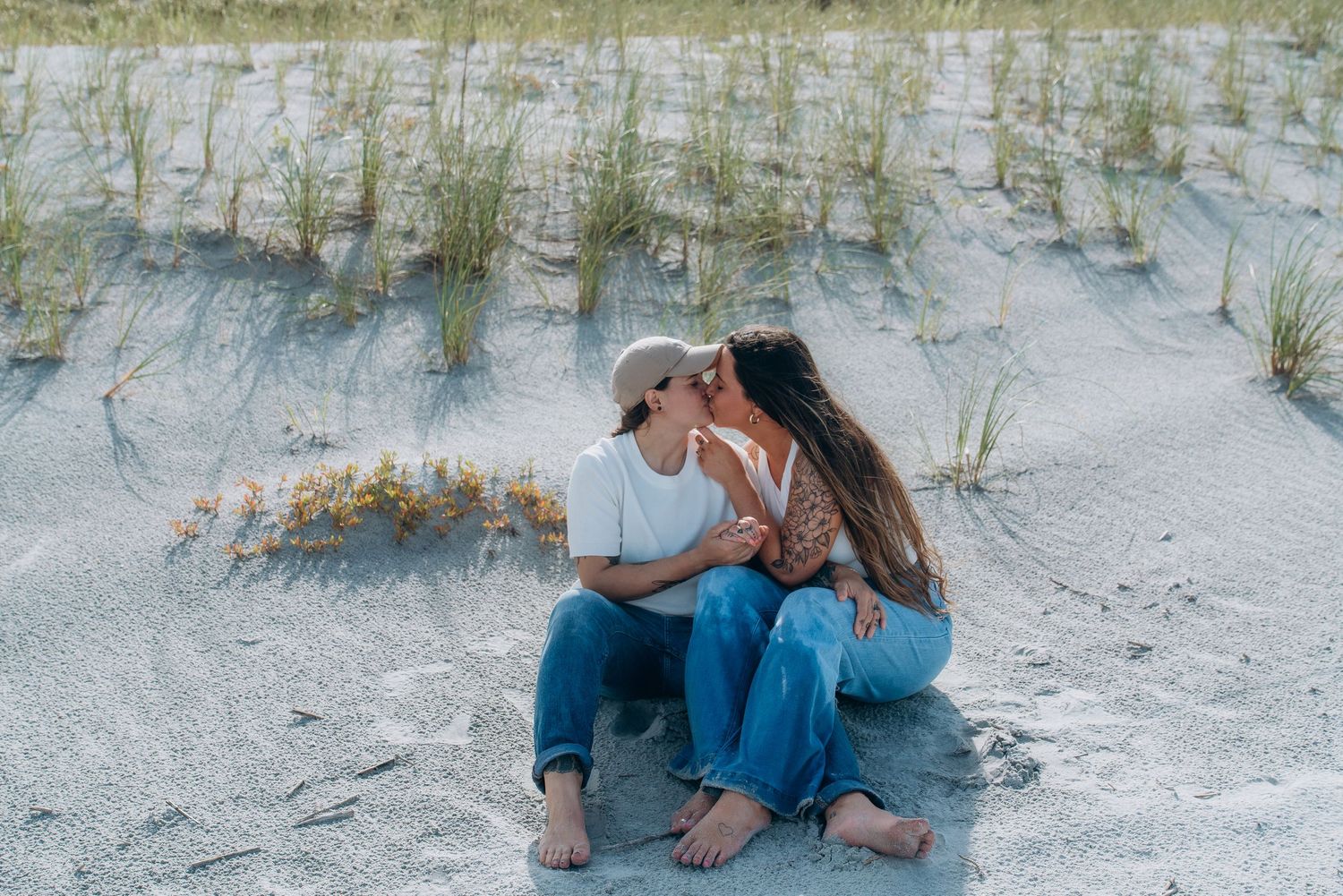 Couple relaxing together on white sand beach with sea grass in the background.