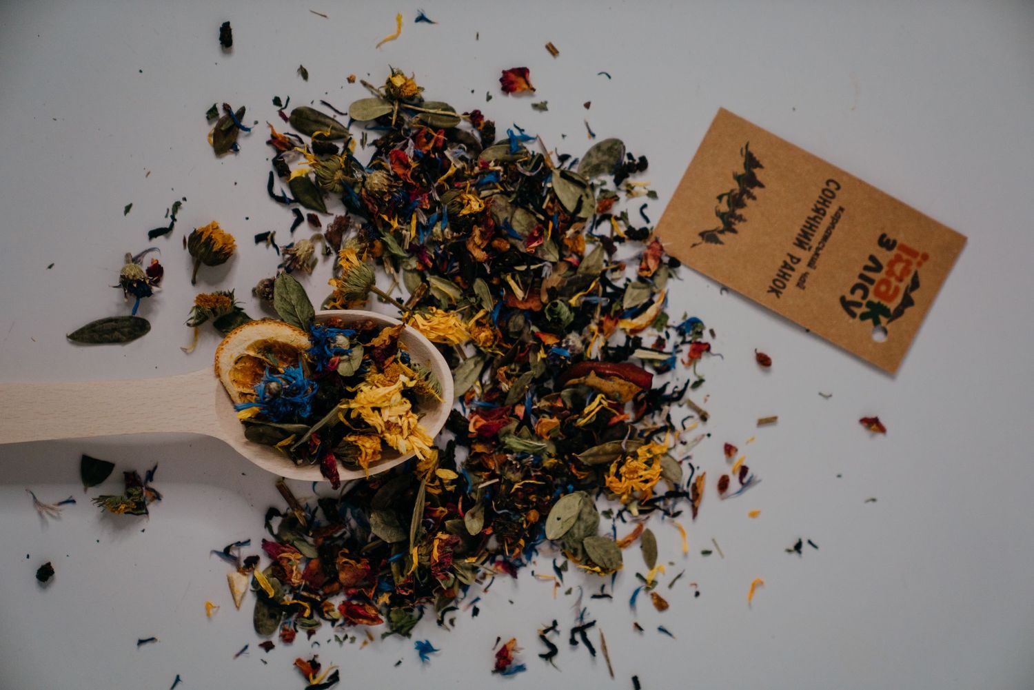 Colorful loose leaf herbal tea blend with dried flowers and spices scattered around a wooden spoon.