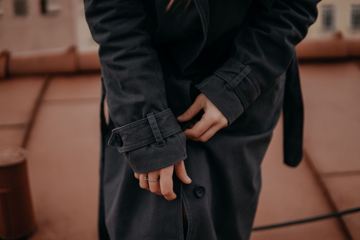 Close-up of woman adjusting dark trench coat sleeve cuff on rooftop.