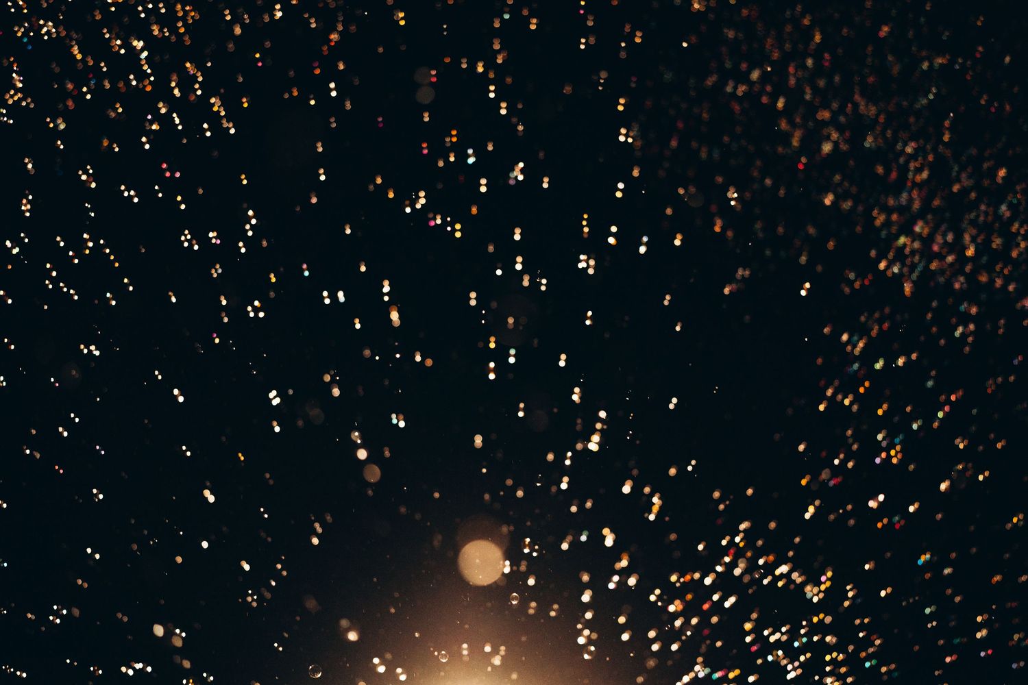 Hundreds of glowing golden sky lanterns float against a dark night sky, creating a magical bokeh light display.