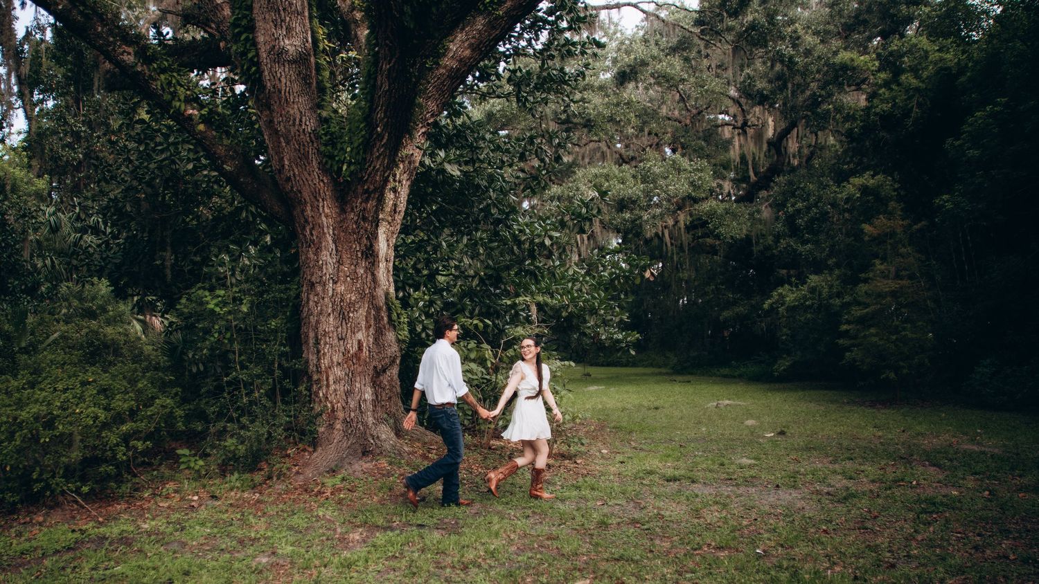 A couple strolling beneath a majestic oak tree in a serene garden setting.