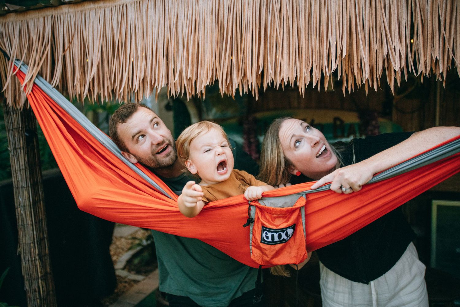 Candid moments of joy and laughter shared in an orange hammock beneath a thatched roof.
