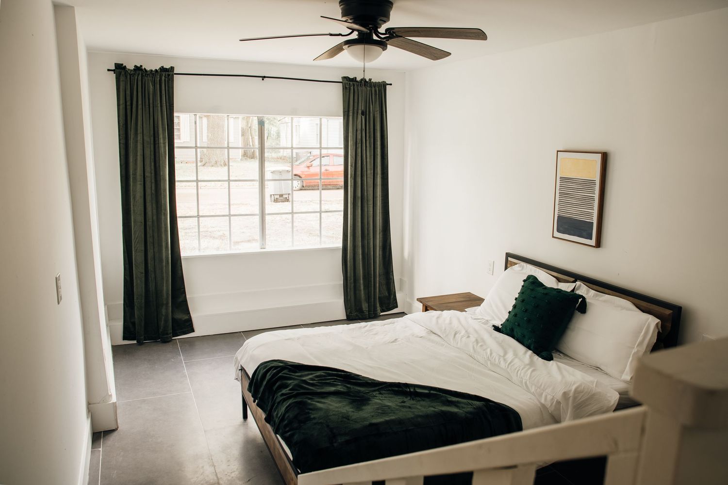 Modern bedroom with white bed, green curtains, ceiling fan, and large window.