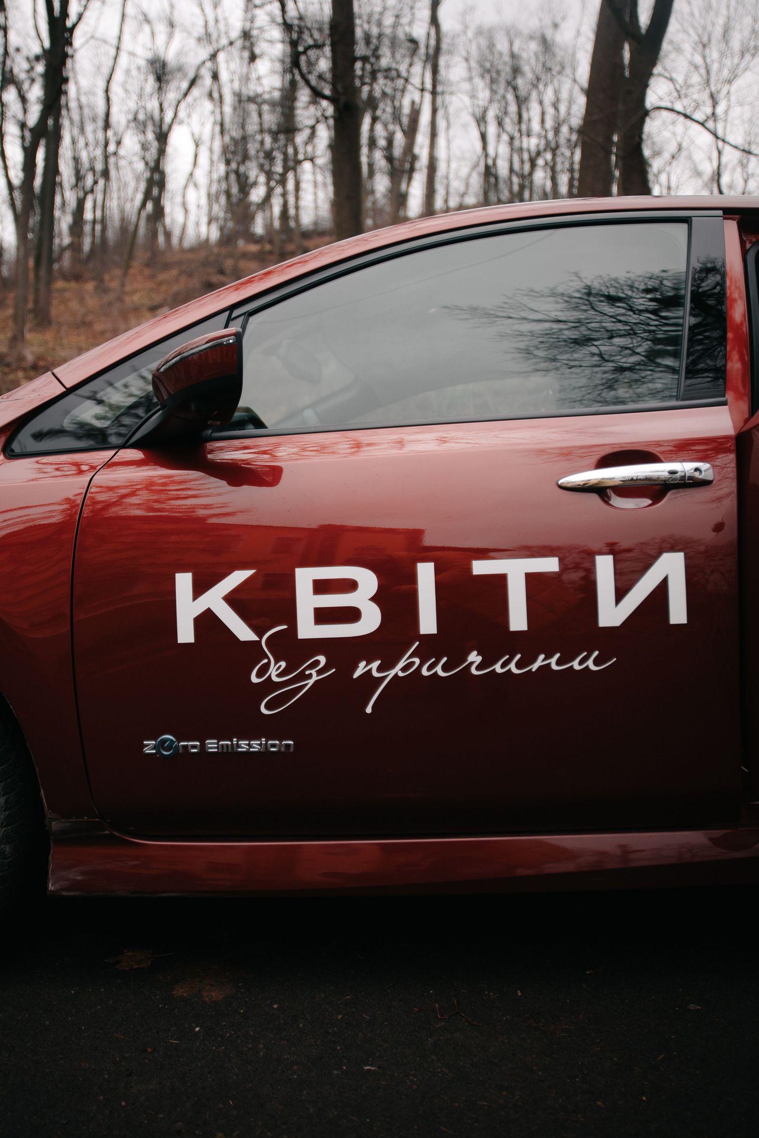 A red car door displays the Ukrainian text KВІТИ без причини meaning flowers without reason in white lettering.