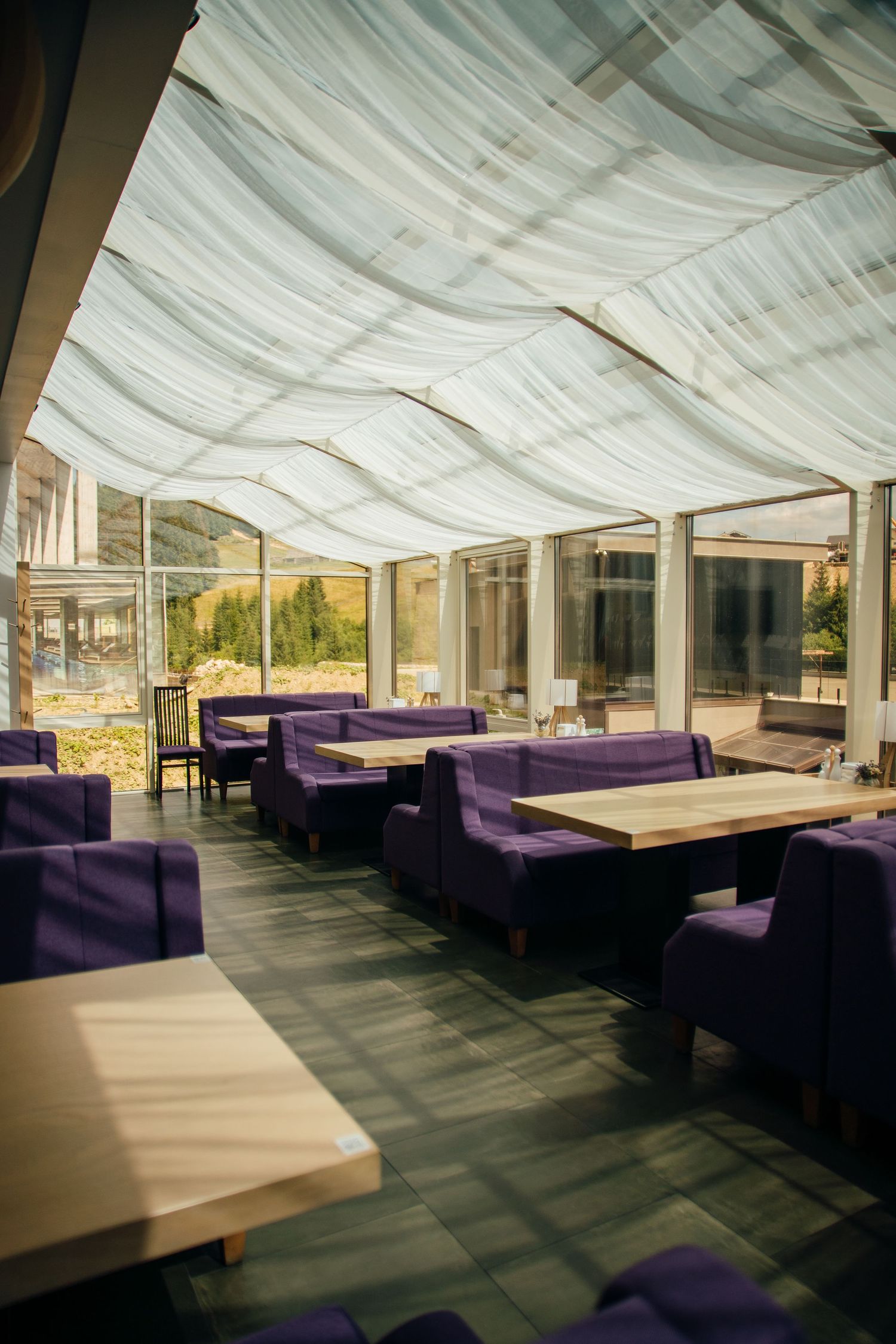 An elegant restaurant interior with purple velvet chairs, wooden tables, and draped ceiling.