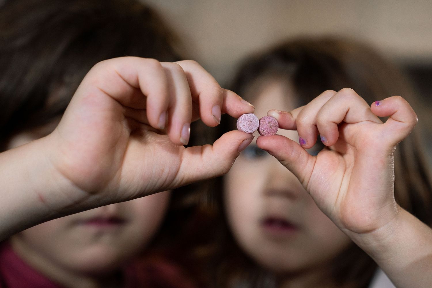 Two children holding small pink candies between their fingers in a close-up shot.
