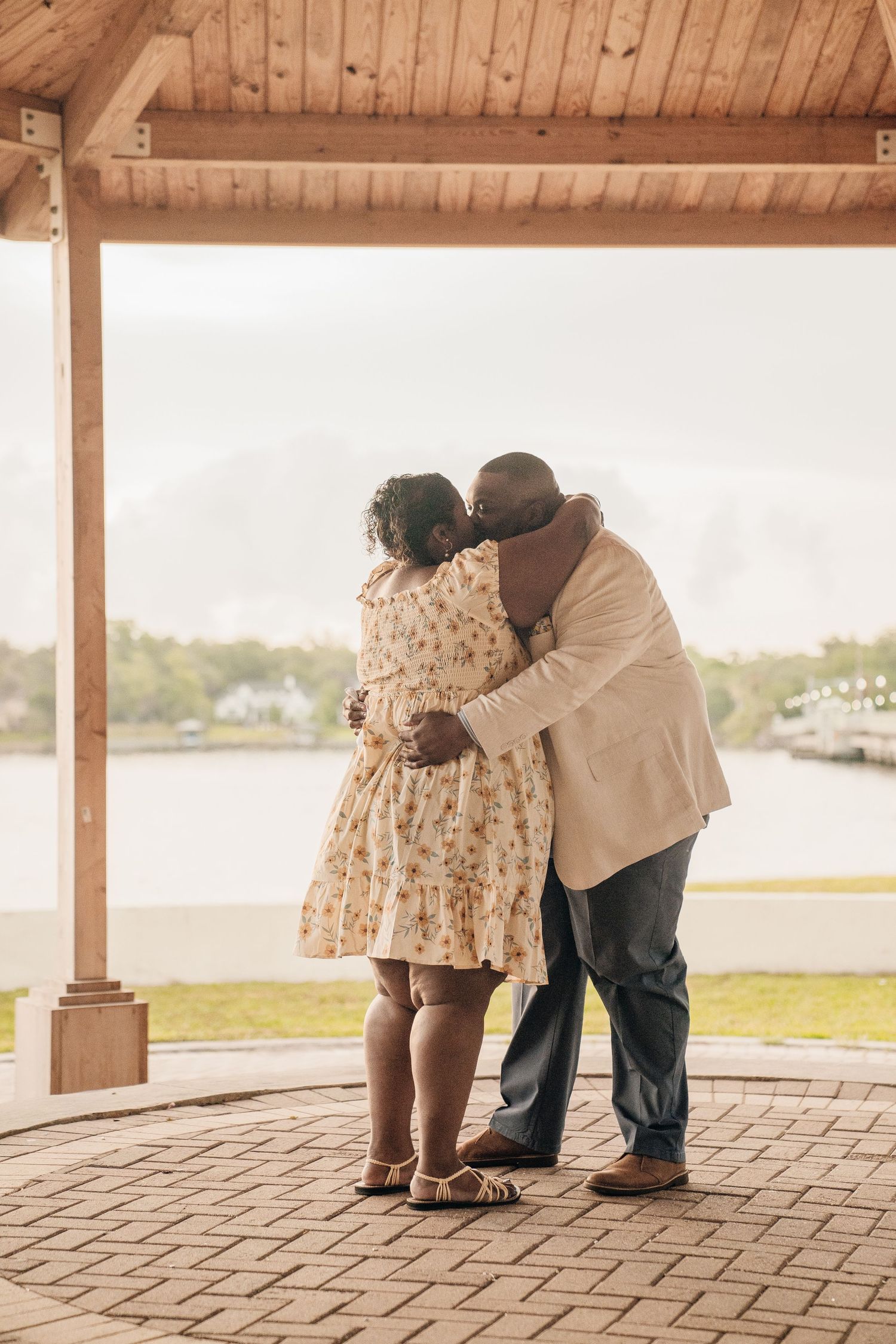 A tender embrace under a wooden gazebo overlooking the water.