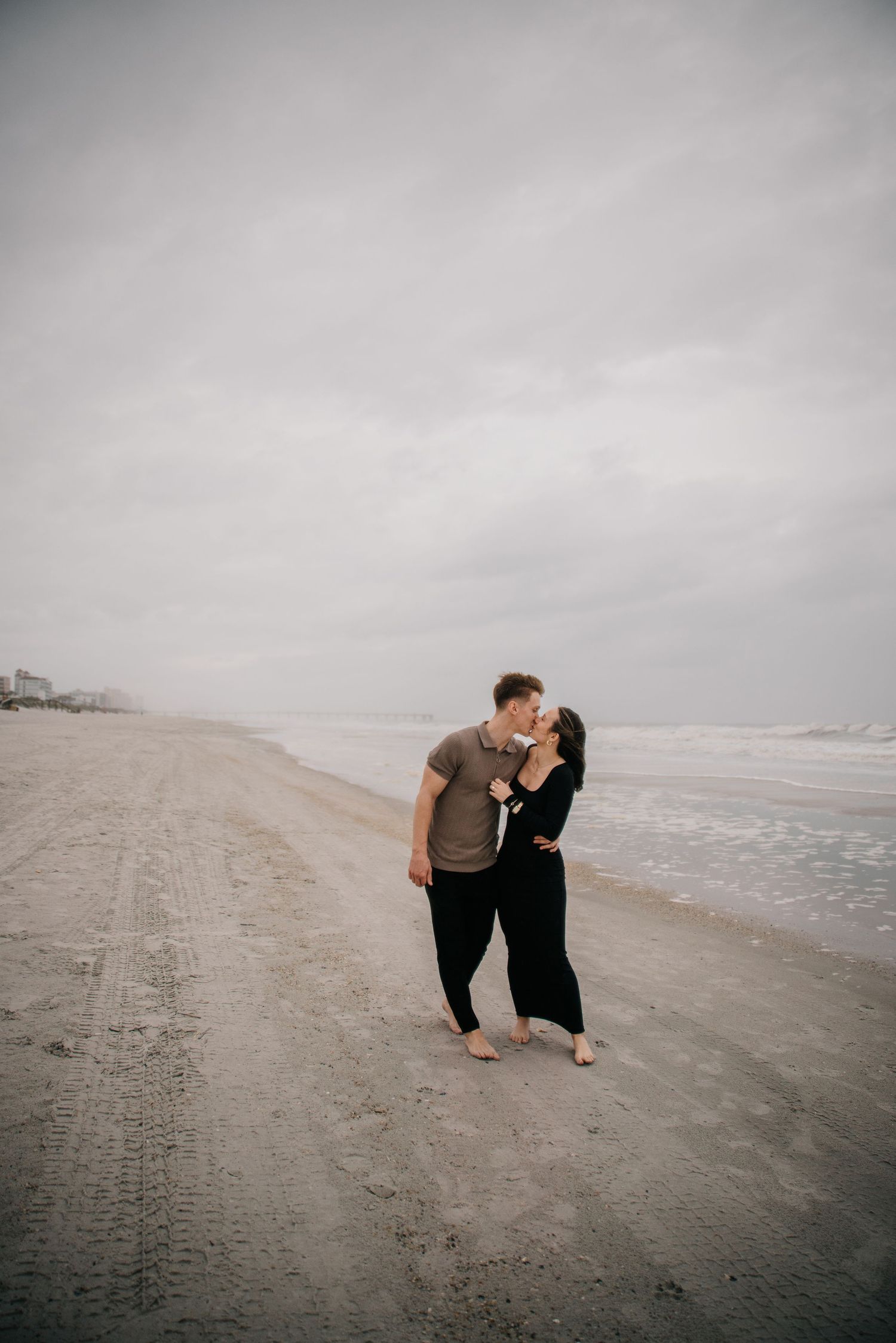 Two people share an intimate moment on a deserted beach with overcast skies.