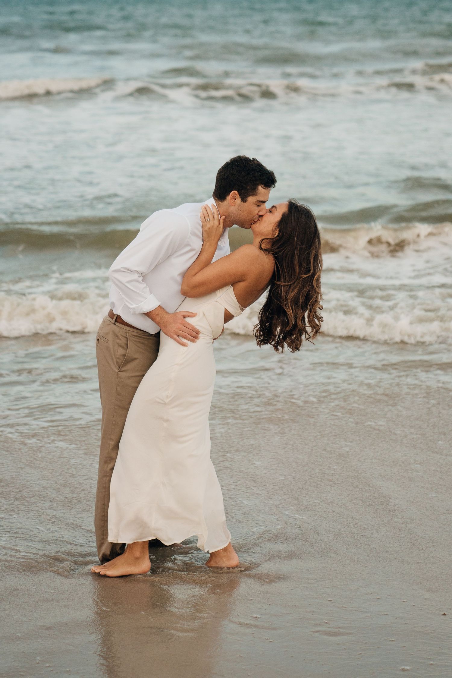 A couple shares a romantic kiss at the ocean's edge.