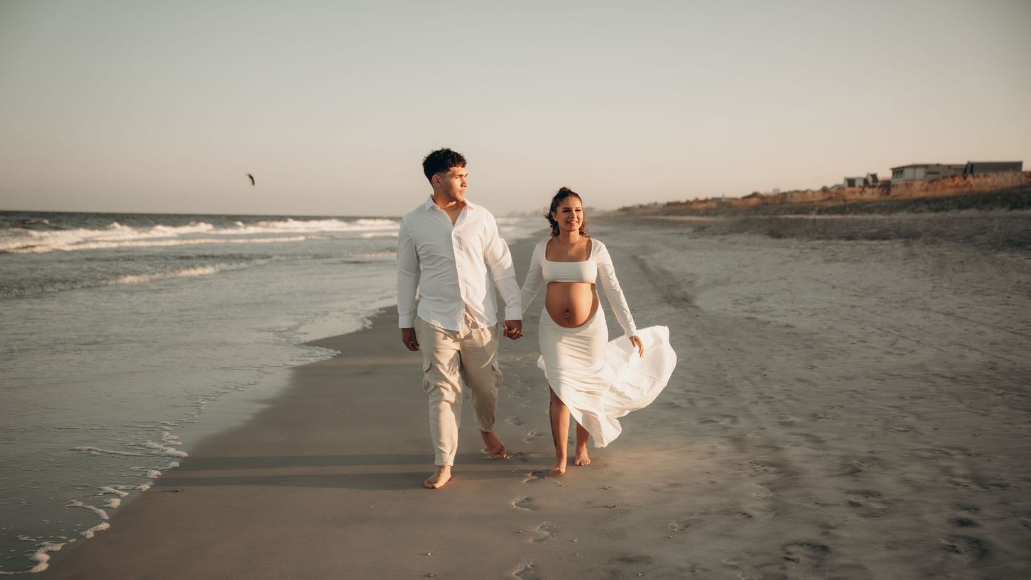 A panoramic beach scene at sunset with a couple walking along the shoreline.