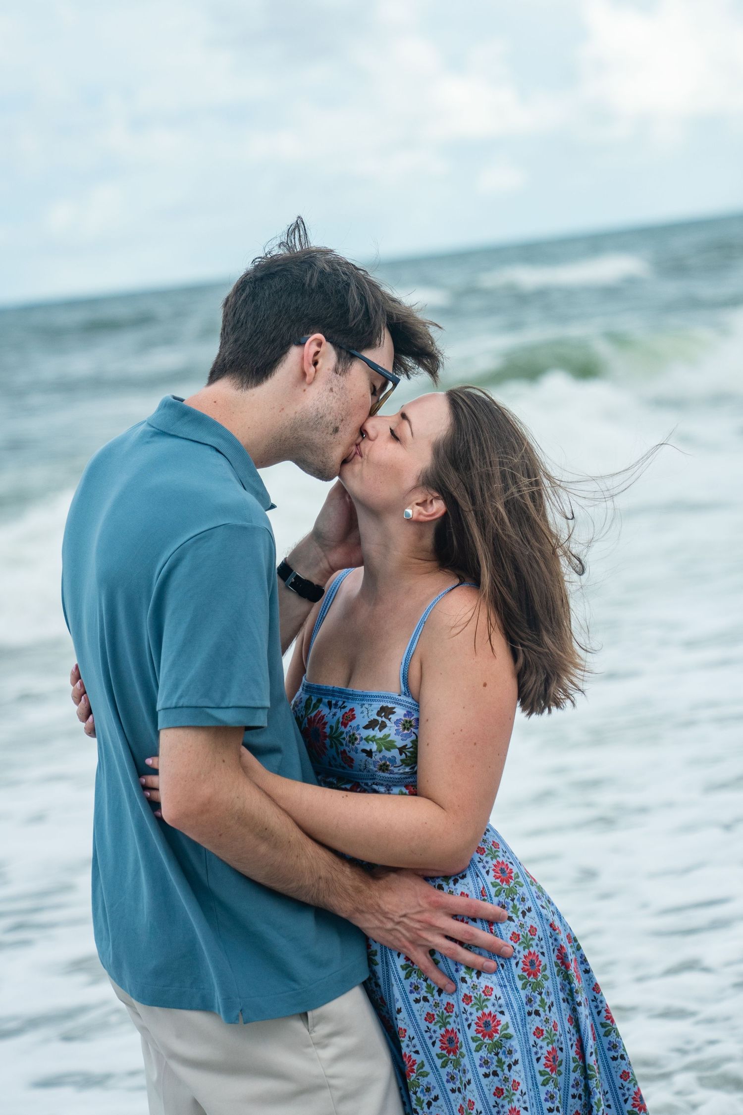 A couple embraces and shares intimate moments along the beach with ocean waves in the background.