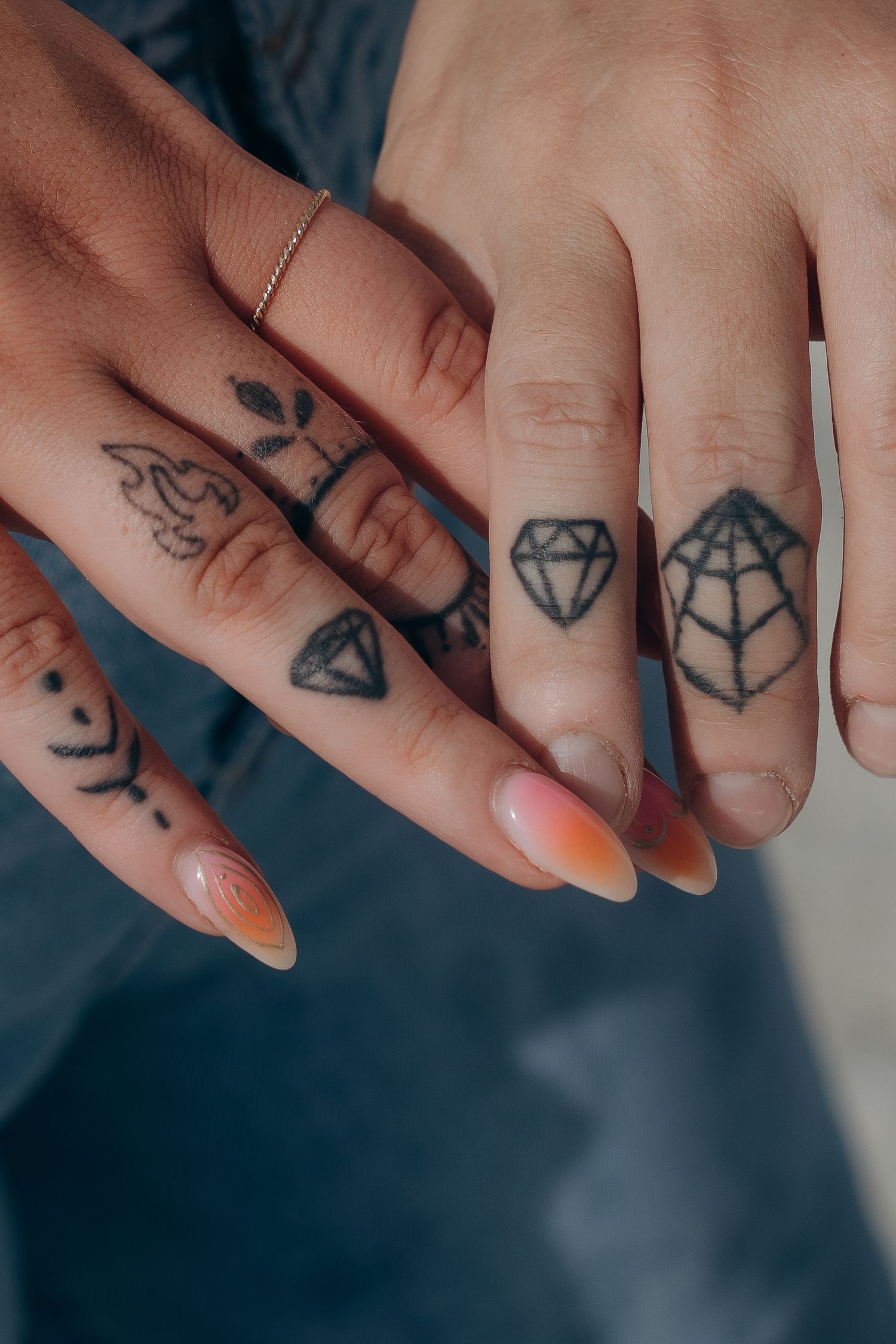 Close-up of fingers with small geometric and diamond tattoos and orange nail polish.
