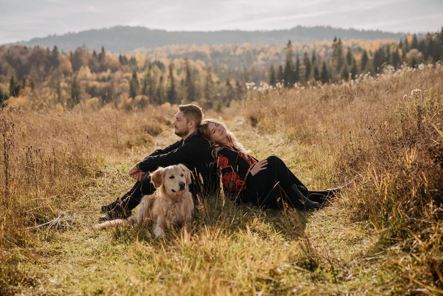 Couple relaxing in autumn meadow with their golden retriever dog among tall grass.