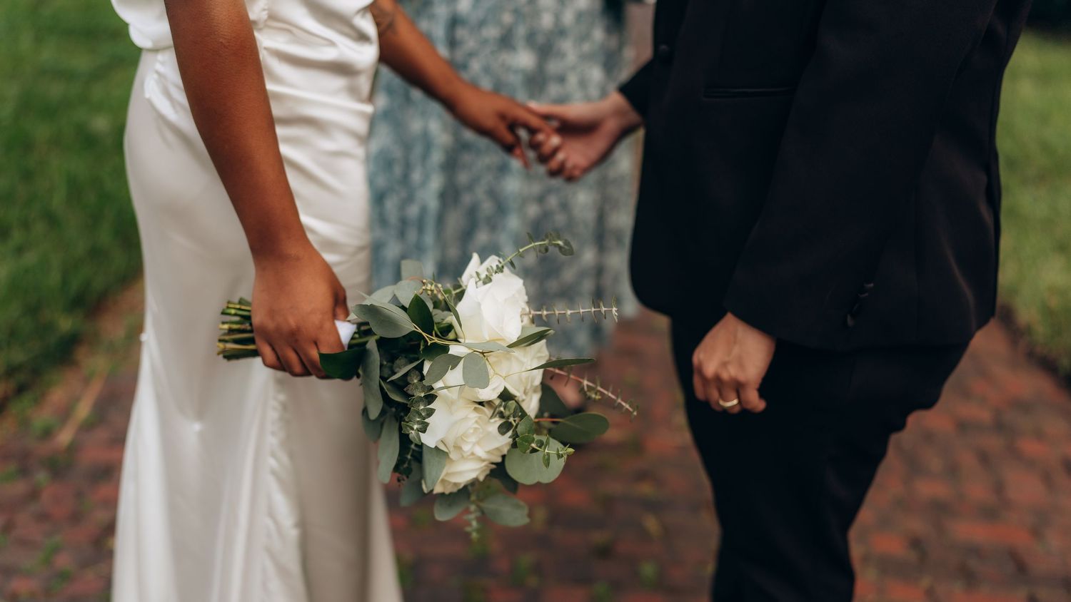 A close-up of wedding attire and white floral bouquet against brick pathway.