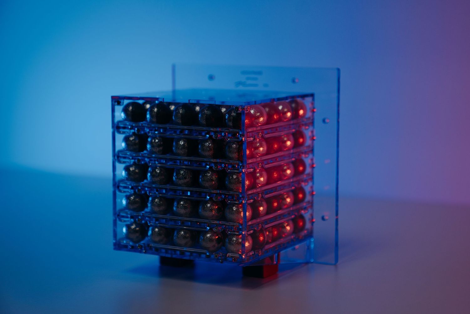 Illuminated LED cube display with red lights in a clear acrylic case against a blue-purple background.