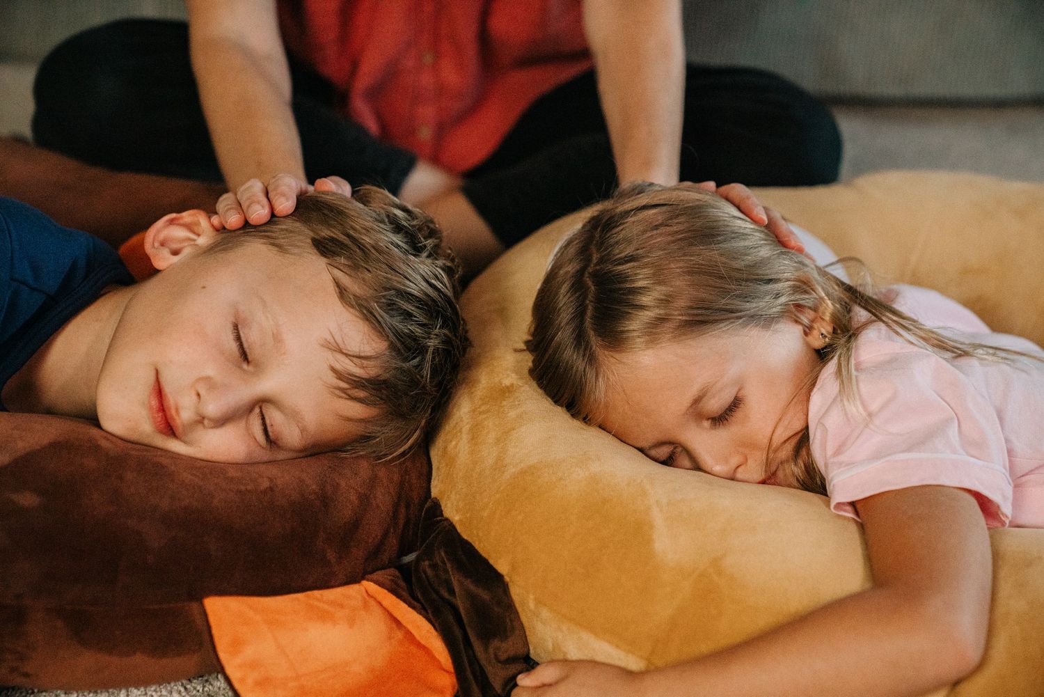 Two children sleeping peacefully on large brown bean bag cushions.