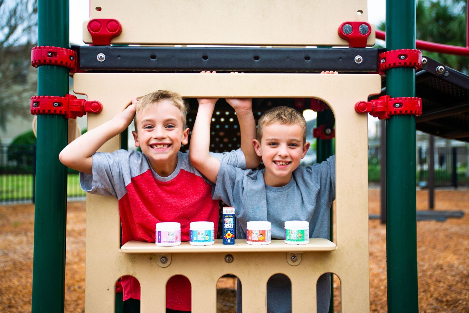 Two smiling boys playing on a colorful playground structure with paint cans displayed on a wooden shelf.