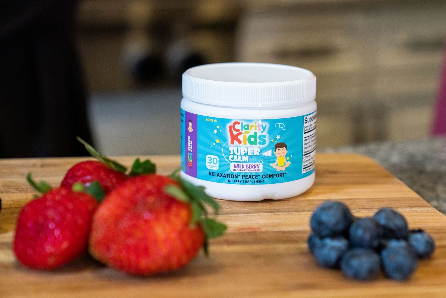 Kids R Kids Super Calm supplement jar on cutting board with fresh strawberries and blueberries.