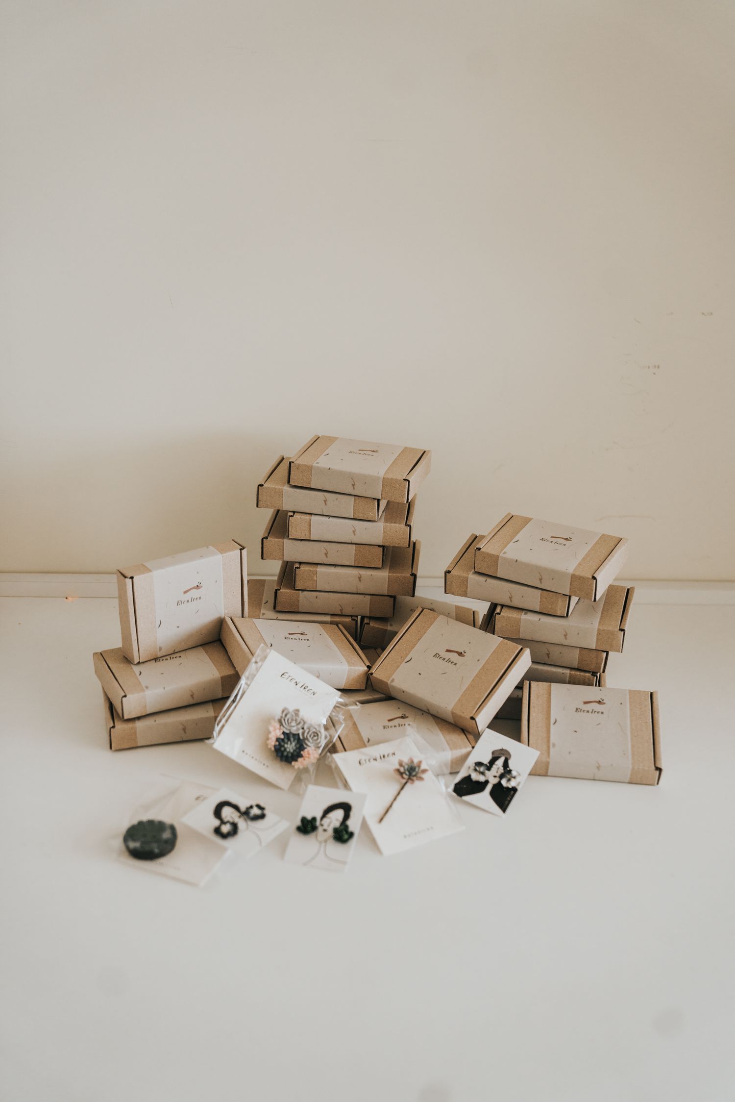 Stack of kraft cardboard boxes with handmade jewelry pieces displayed on white surface.
