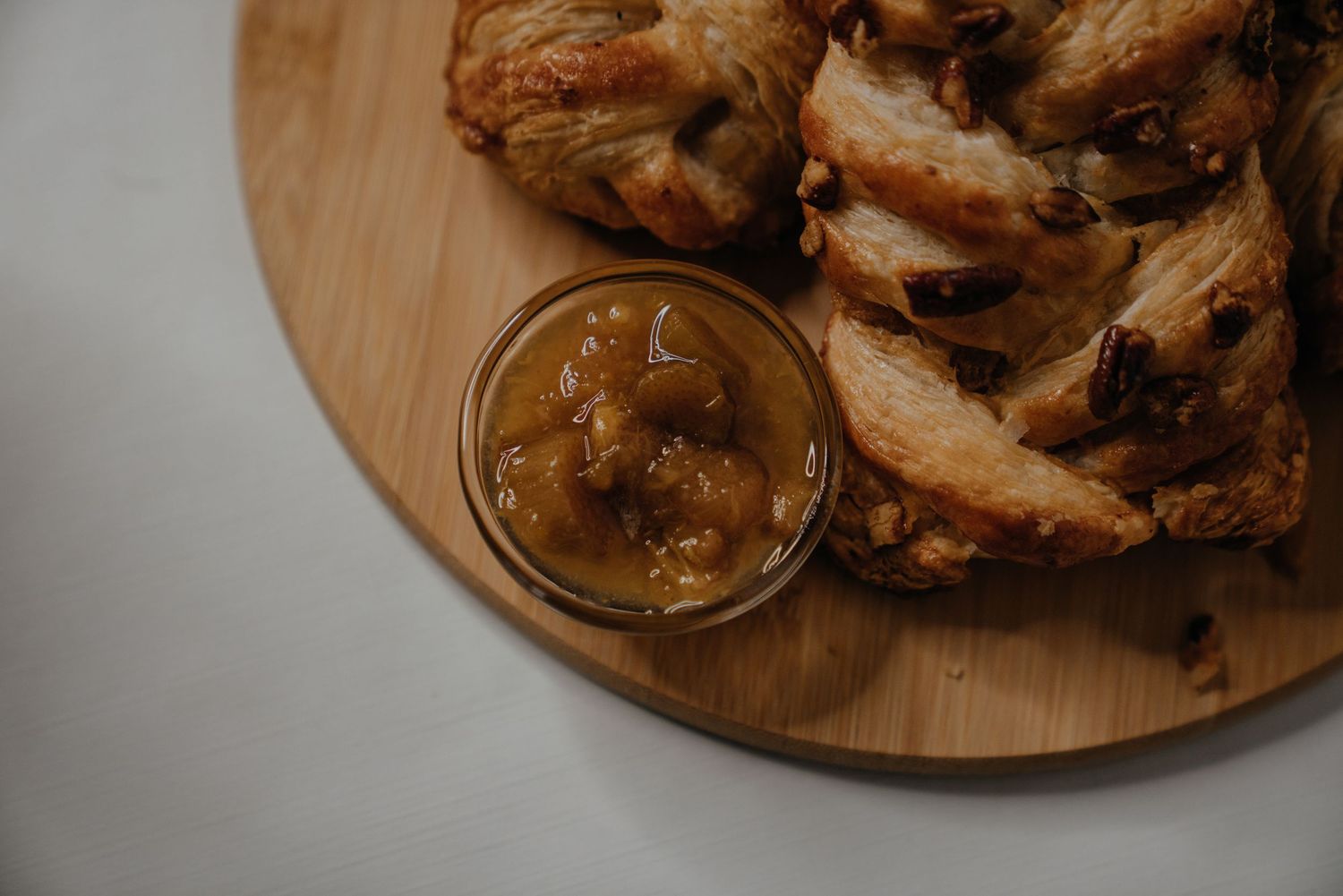 Freshly baked pastry with chocolate chips on a wooden board served with a small glass jar of caramel sauce.