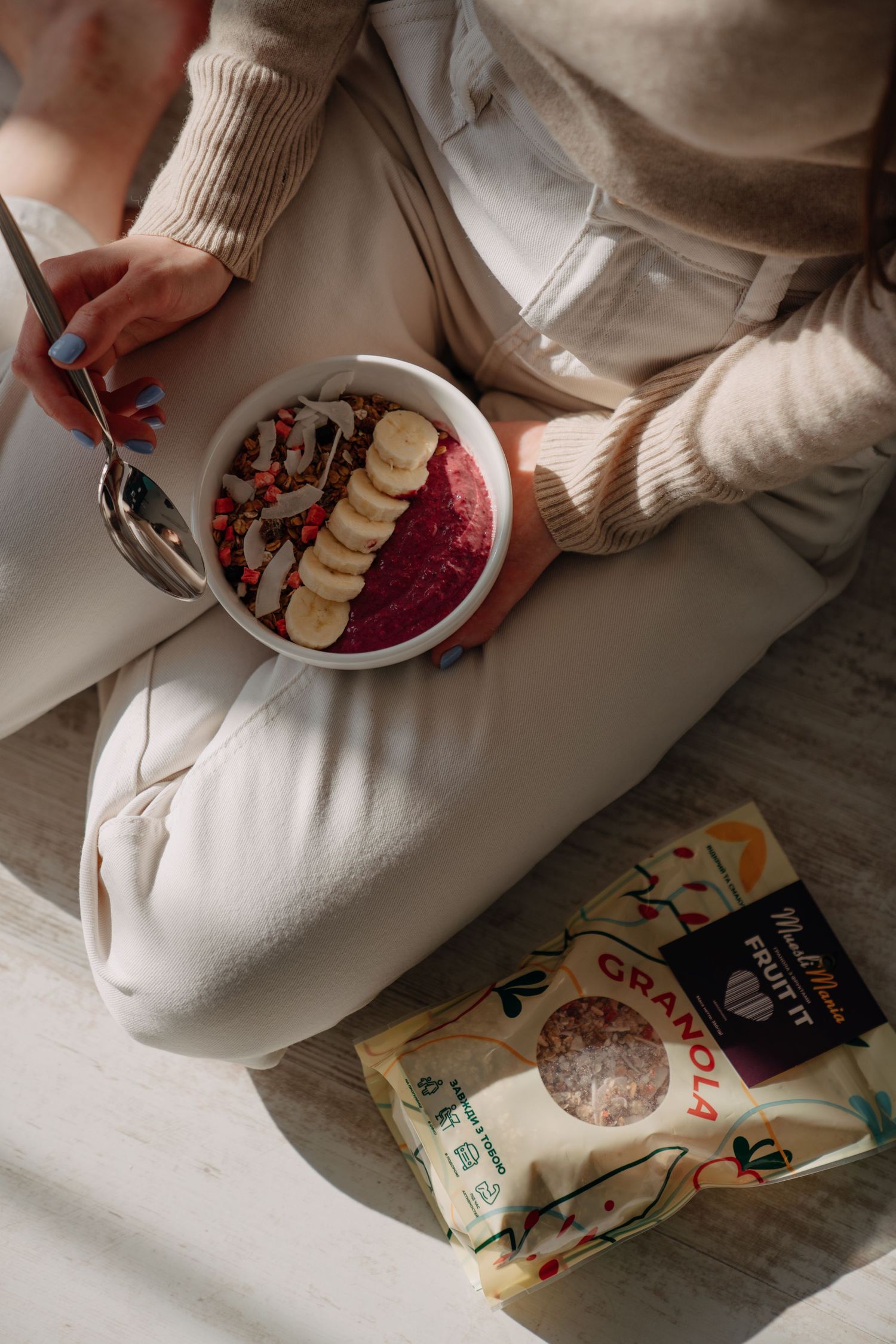 Overhead view of person holding a smoothie bowl with granola topping next to a MuesliMania bag.