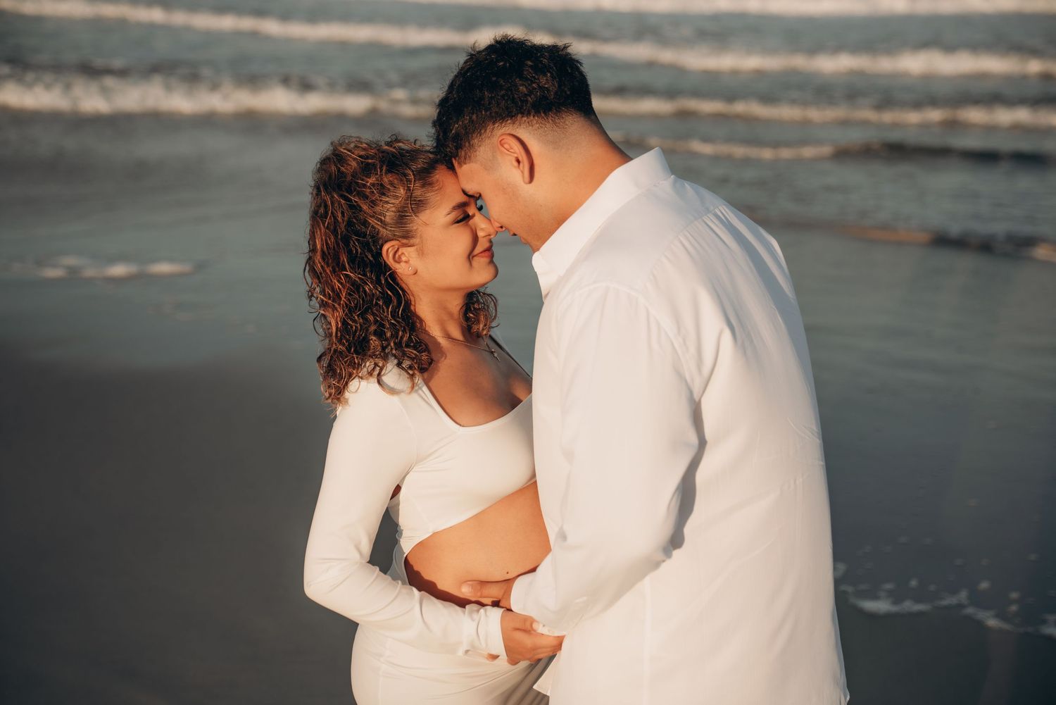 Romantic beach maternity photos captured at sunset with waves in the background.
