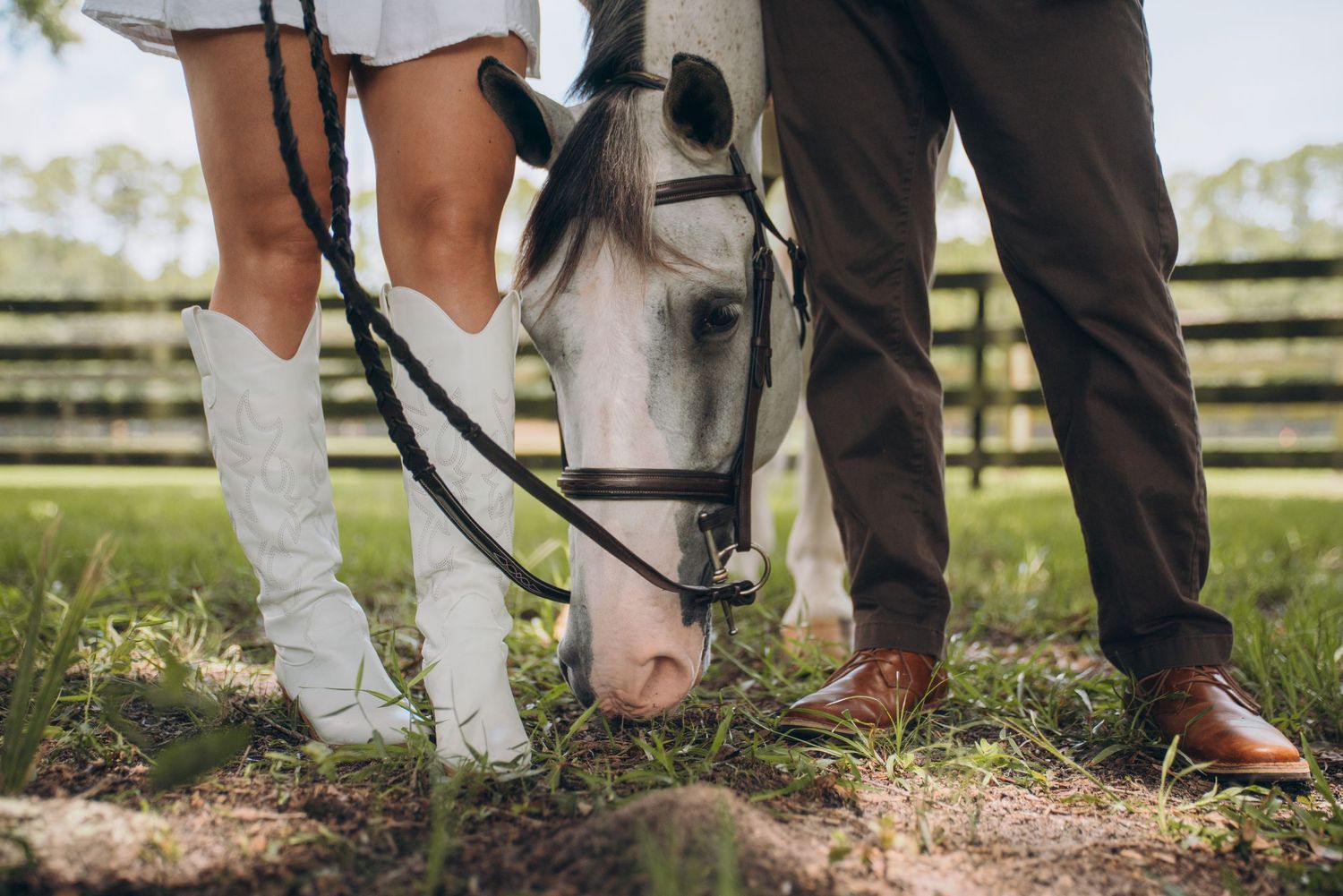 A couple stands close to their white horse in a peaceful countryside setting.