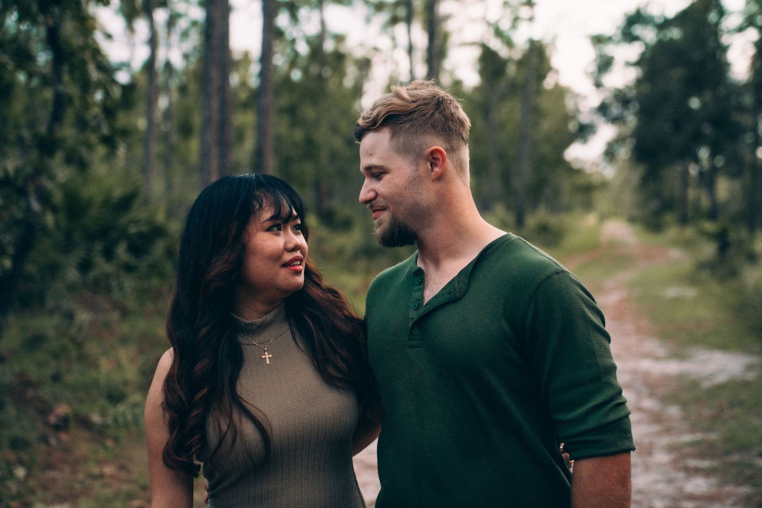 Couple laughing together on outdoor path with pine trees and natural lighting.