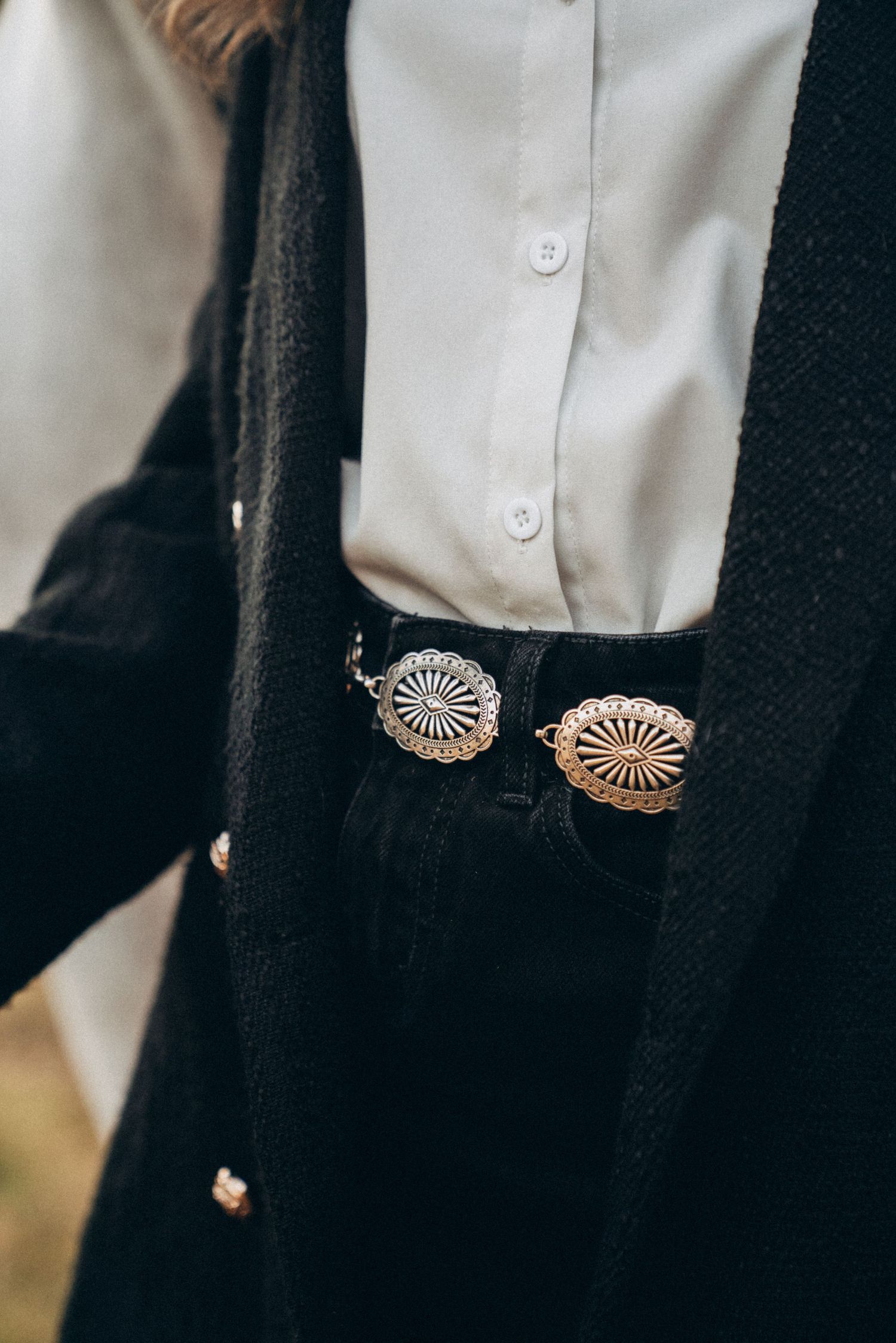 Close-up detail of ornate concho belt with silver medallions against black fabric.
