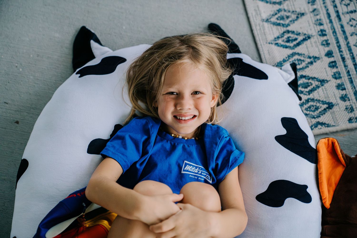 Happy young girl smiling while lying on a black and white cow print bean bag pillow indoors.