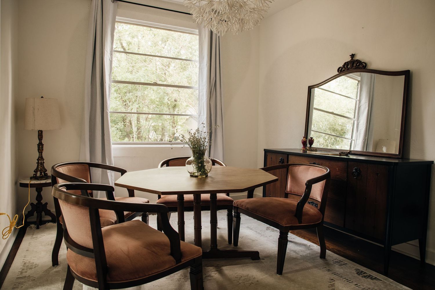 A classic dining room with round wooden table, brown chairs, mirror, and chandelier.