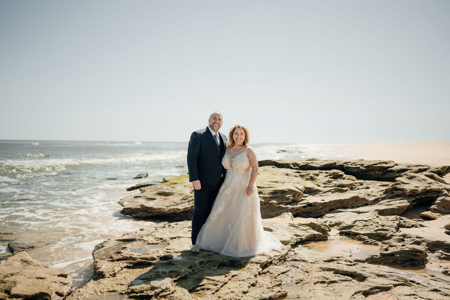 Wedding couple posing on rocky coastal cliffs with ocean views.