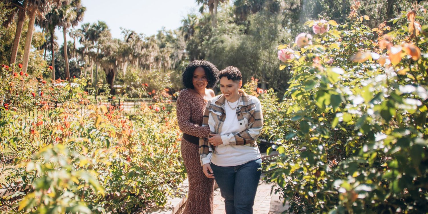 A couple walks through a garden with blooming flowers and greenery.