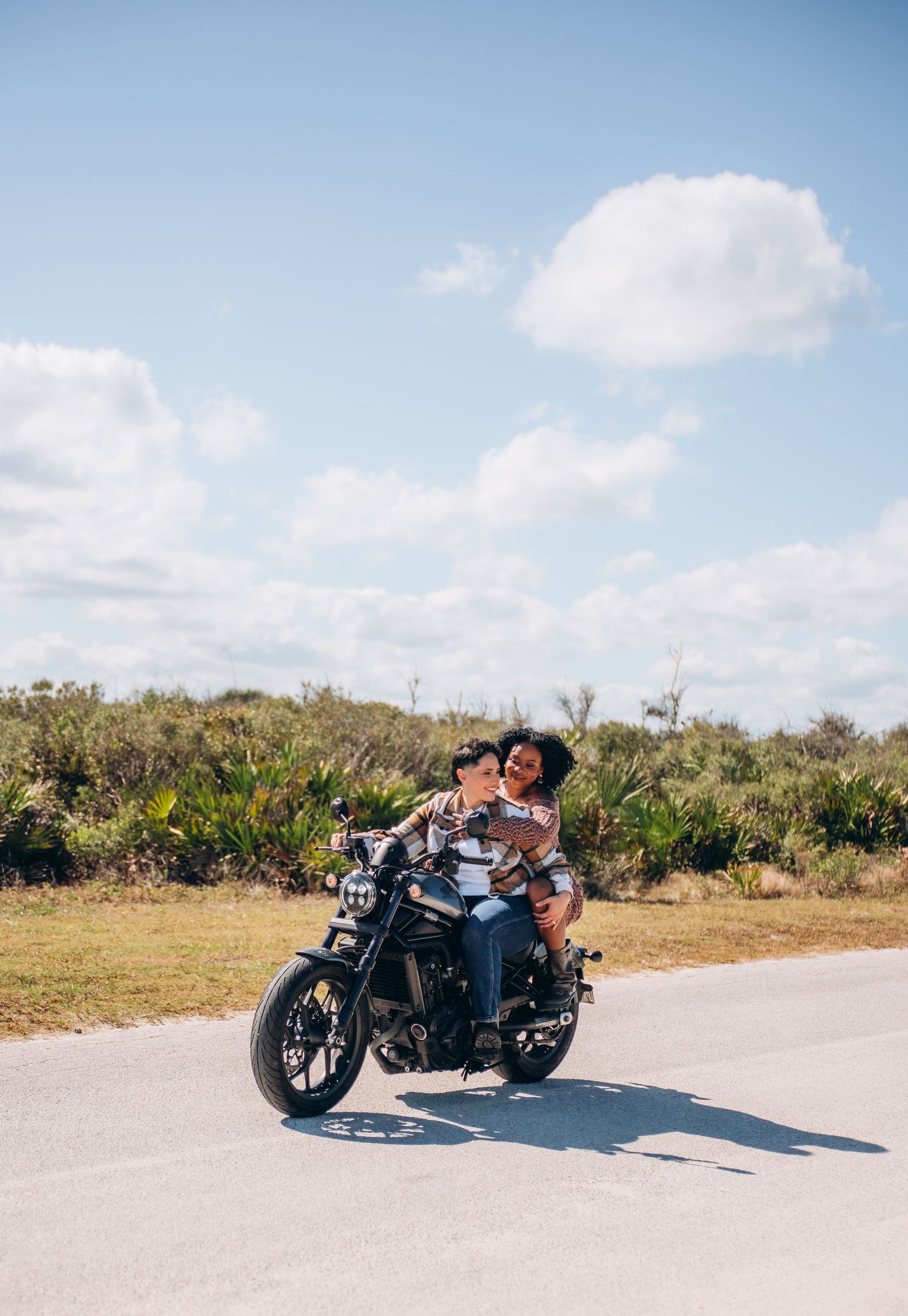 A motorcycle parked on a sunny road with blue skies and coastal vegetation in the background.