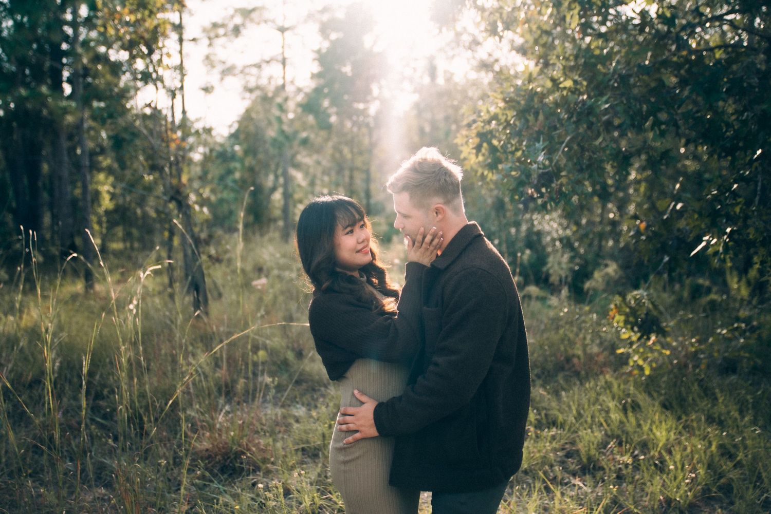 Romantic couple embraces in a dreamy sunlit wooded setting.
