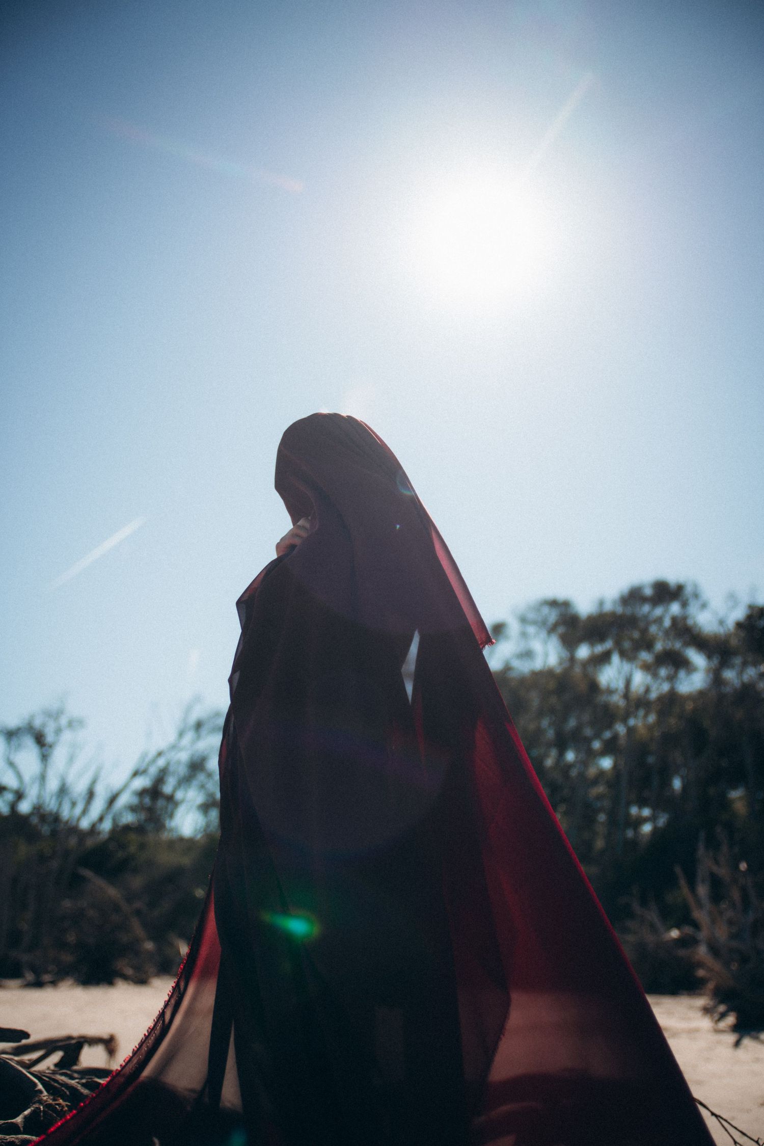 Silhouette of a draped figure standing on a beach under bright sunlight.