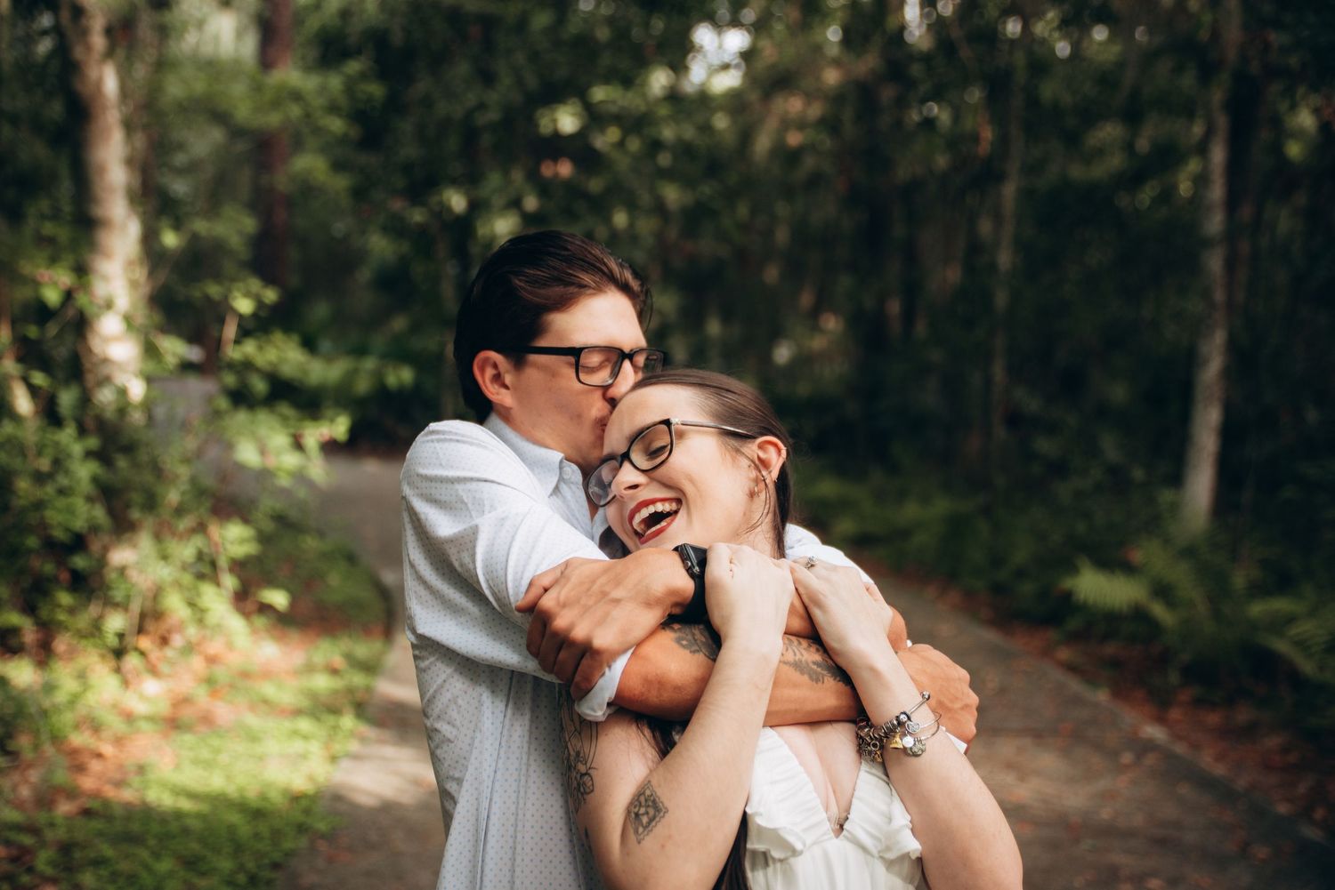 Couple enjoys intimate moments along a tree-lined path near historic home.