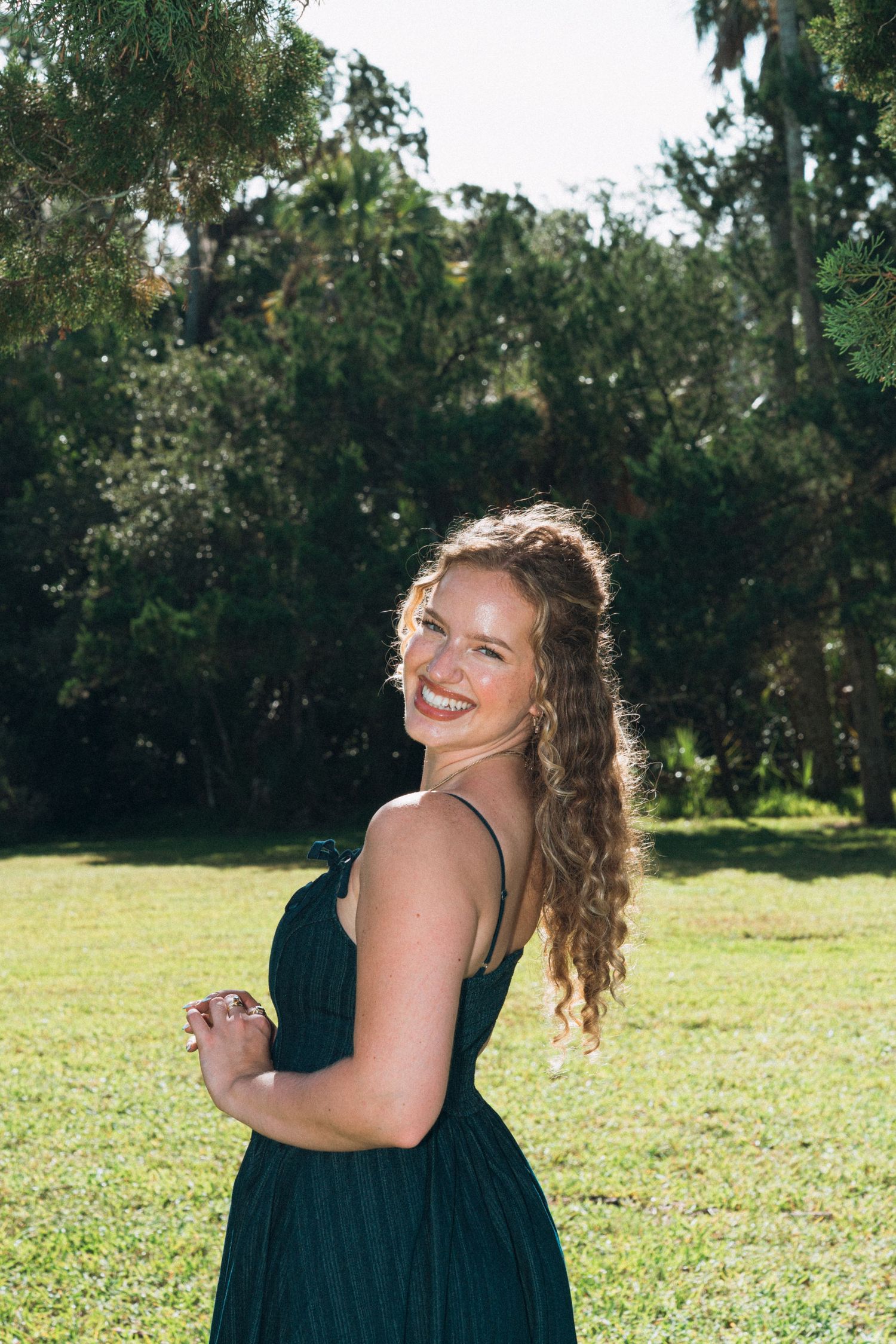 Woman in black dress poses joyfully in a sunny green field.